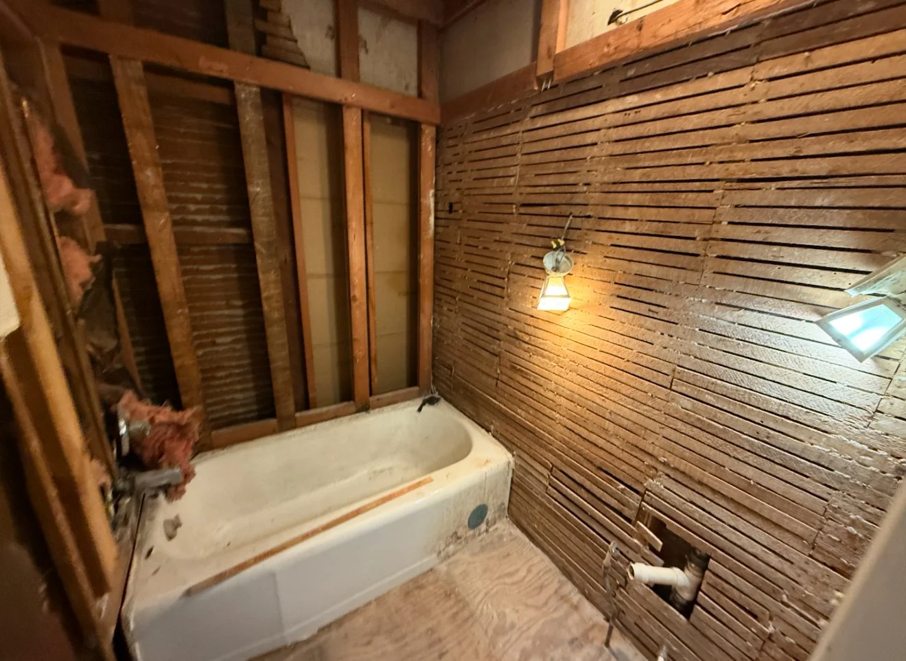 Undeveloped bathroom with exposed wooden framing, an old bathtub, and unfinished walls with insulation and wiring.
