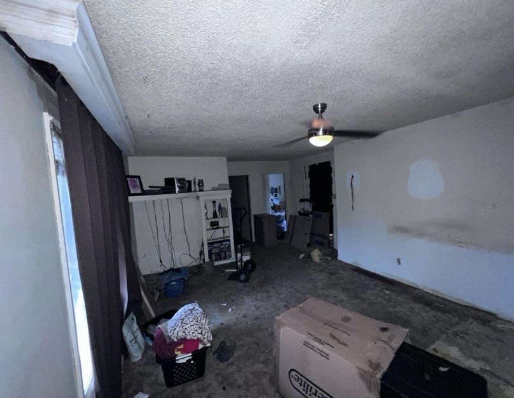 Empty living room with clutter, a ceiling fan, and a window with closed dark curtains.