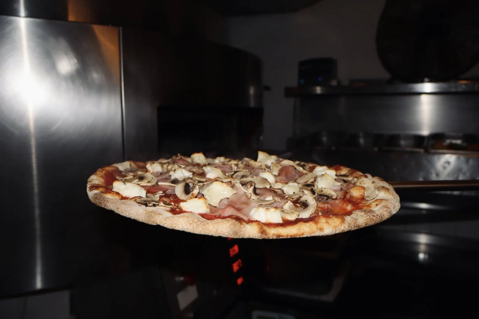 Een pizza met champignons, kaas, ham en tomatensaus die uit een oven komt.