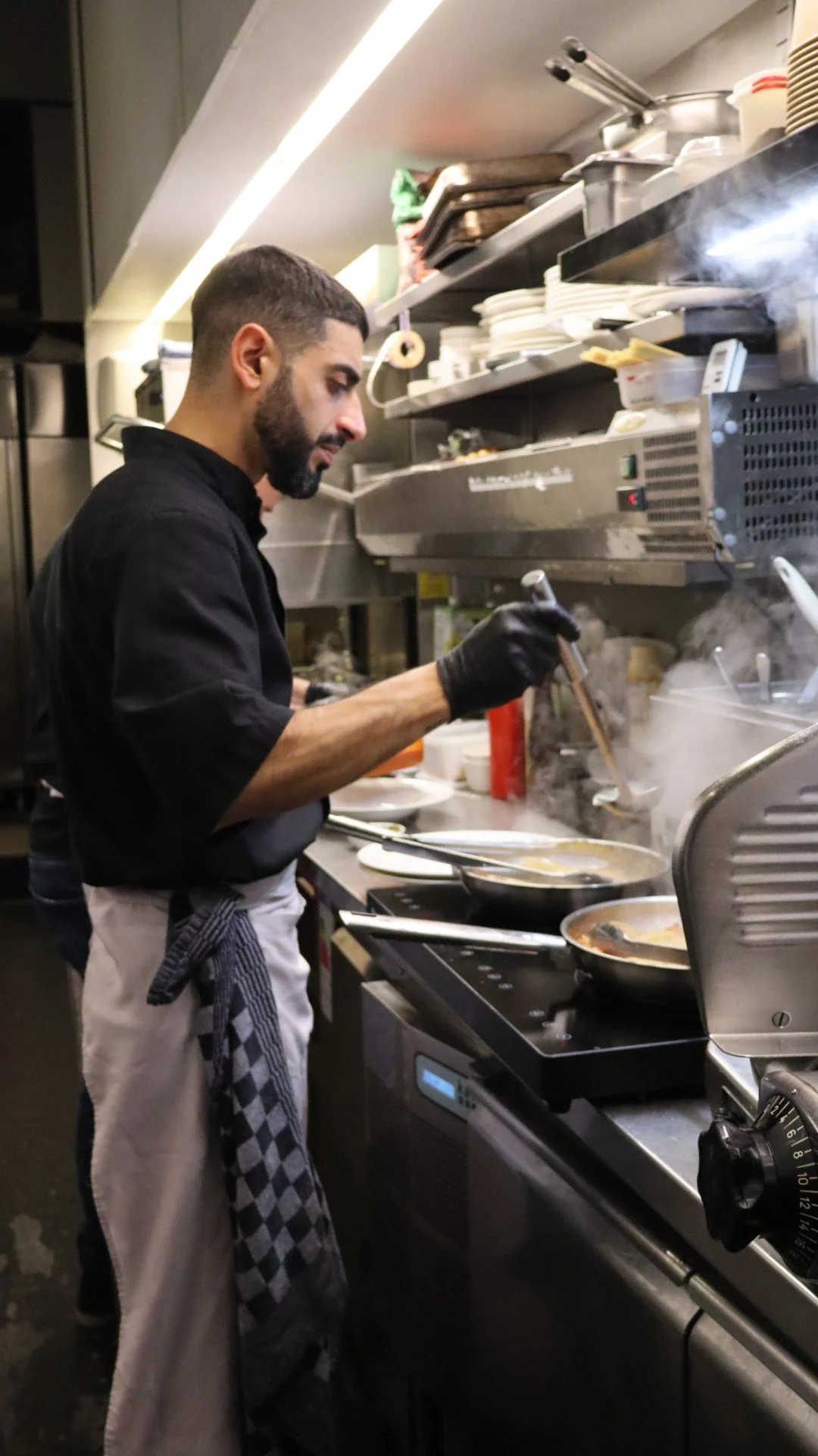 Een man kookt in een professionele keuken met een kookplaat, enzovoort, met dampen die opstijgen.