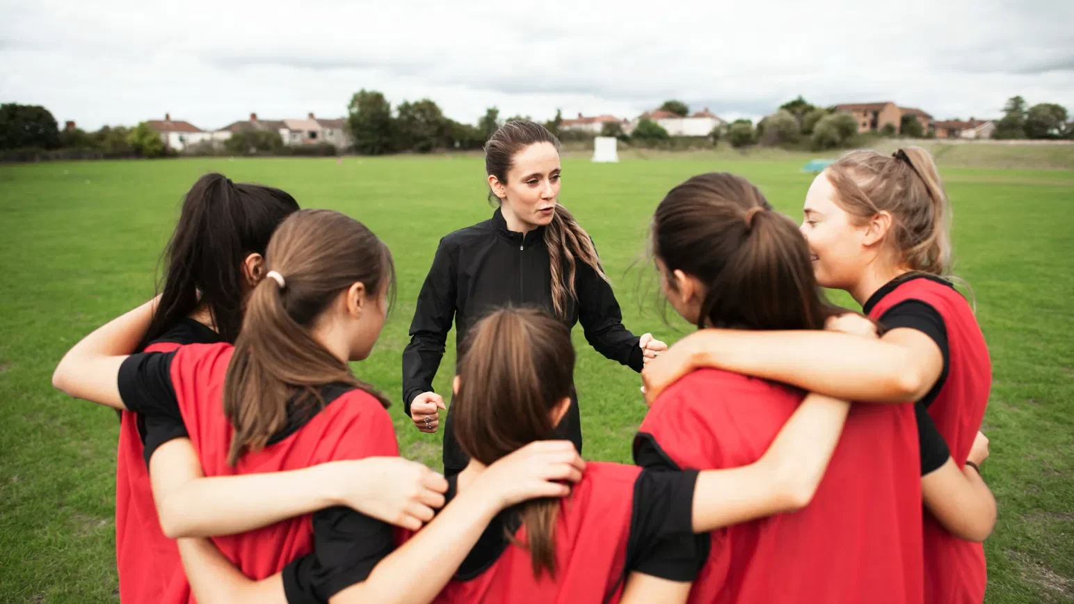 A female soccer coach giving team pep talk to young female players on a grassy field.