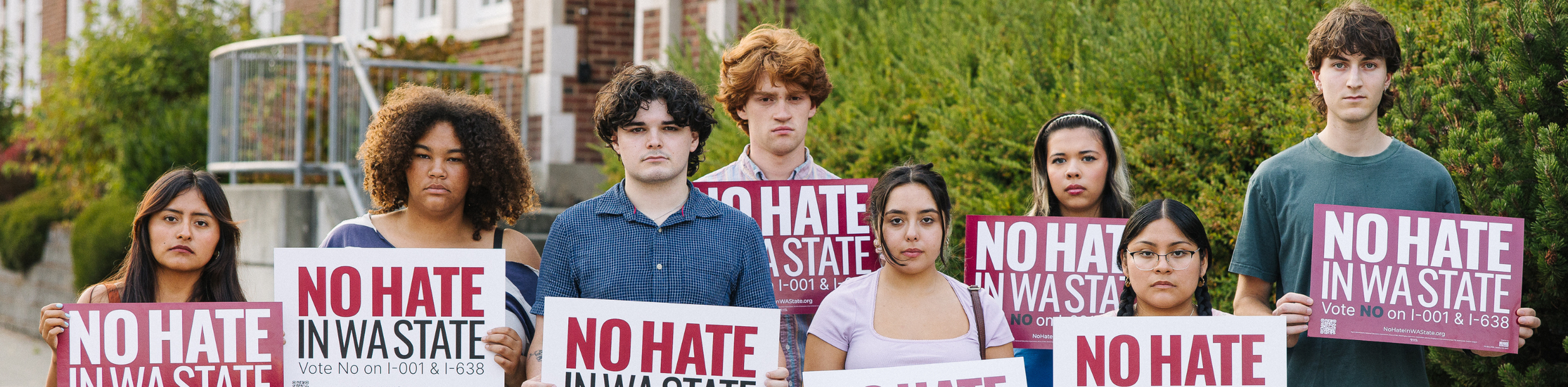 Group of diverse young adults protesting against hate in W state, holding signs that read 'No Hate in WA State' and promoting voting against hate.