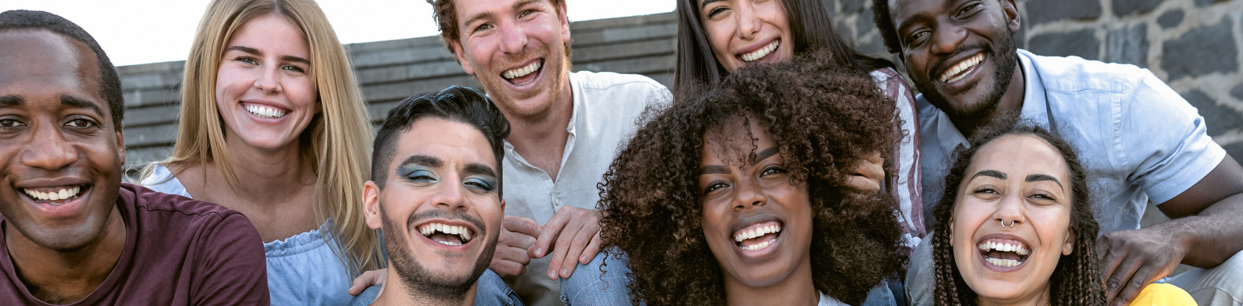 A diverse group of nine young adults smiling and laughing together outdoors.