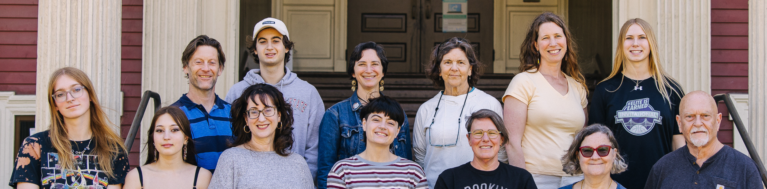Group of people, diverse ages, posing on the steps of a house, smiling, in casual clothing.