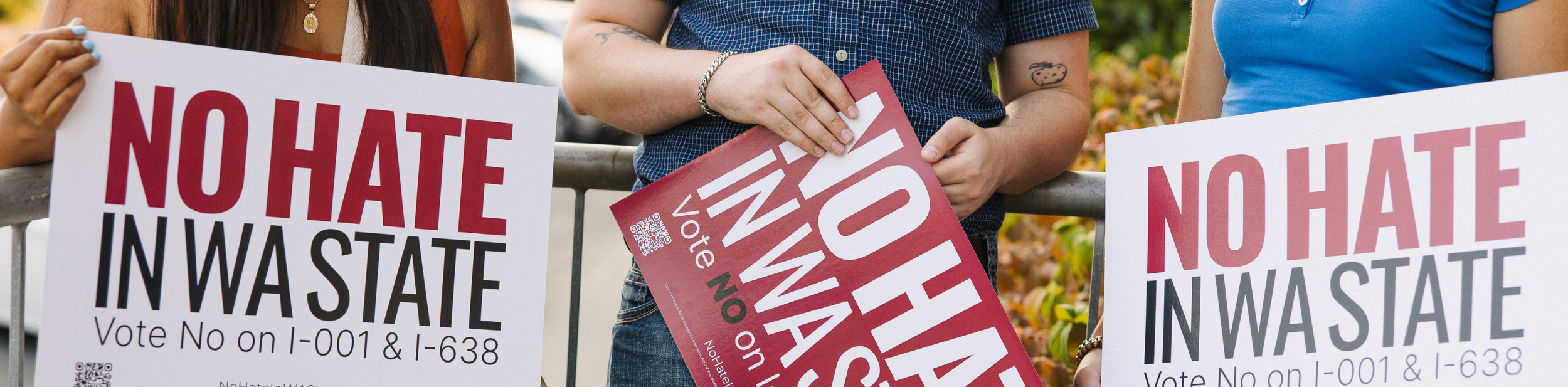 People at a protest holding signs that say "No Hate in WA State" and encourage voting no on propositions I-001 and I-638.