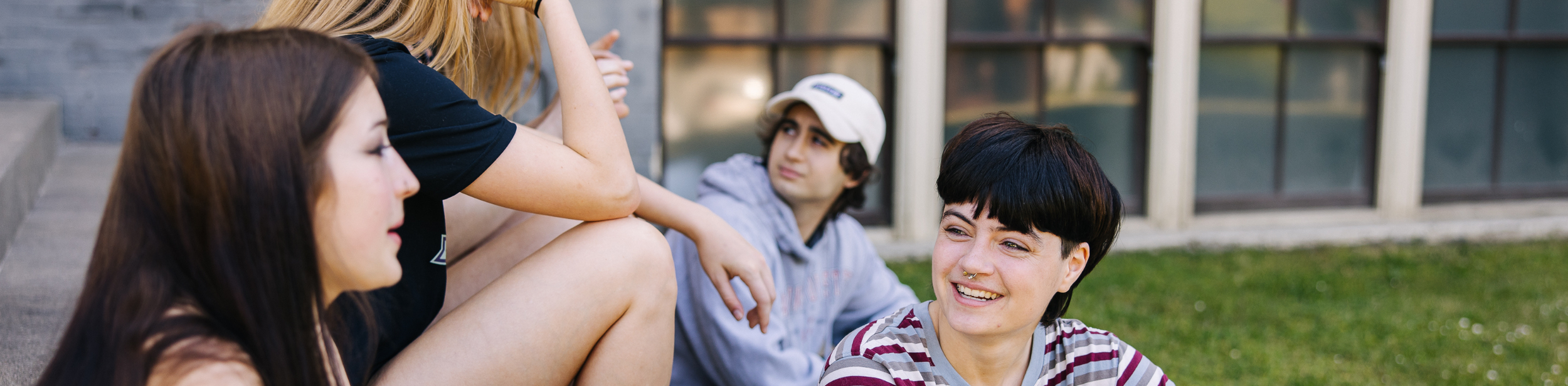 Four teenagers sitting outdoors and talking, with a building in the background.
