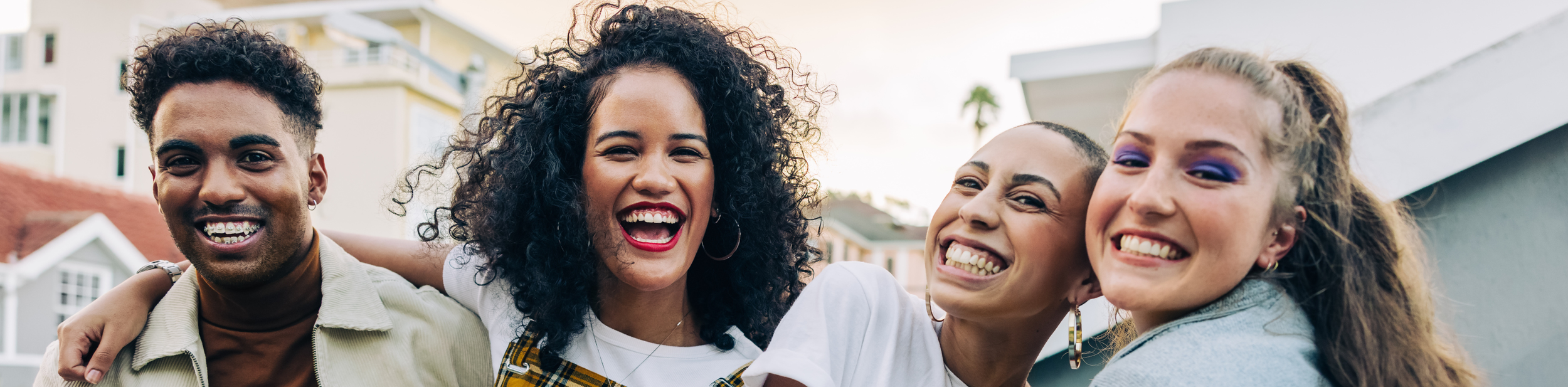 Four friends smiling and hugging outdoors in a neighborhood, enjoying a sunny day.