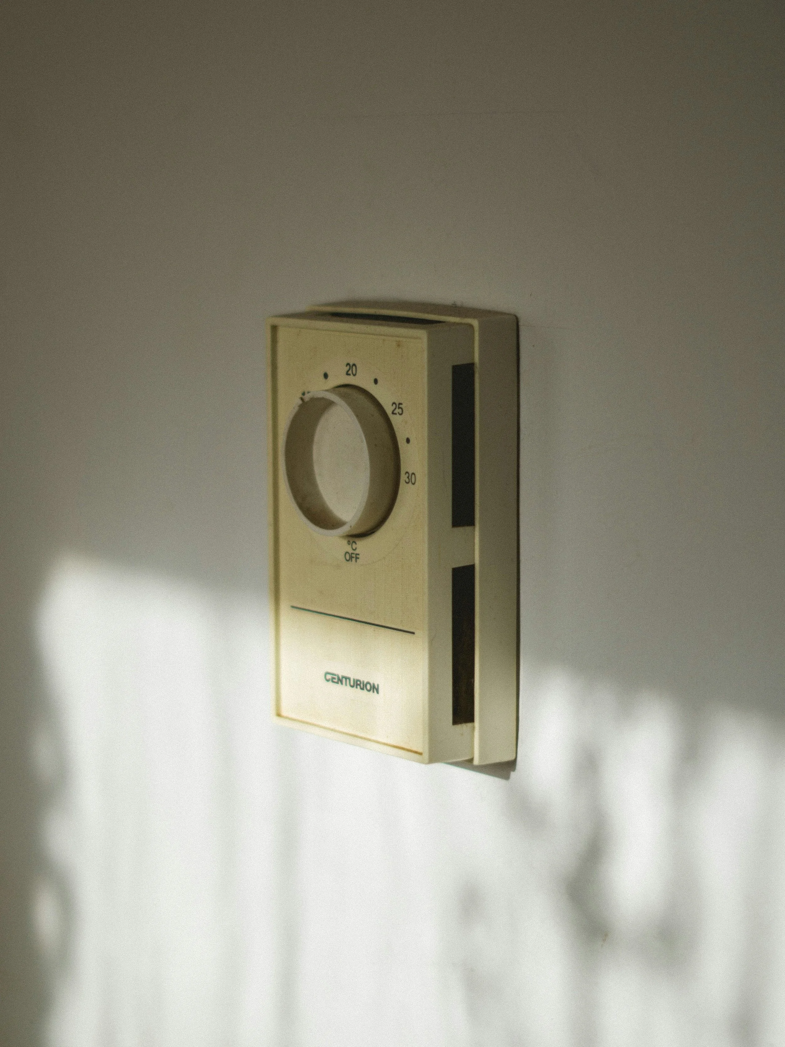 A vintage Centurion thermostat on a white wall, with a round temperature control dial and a black sliding indicator.