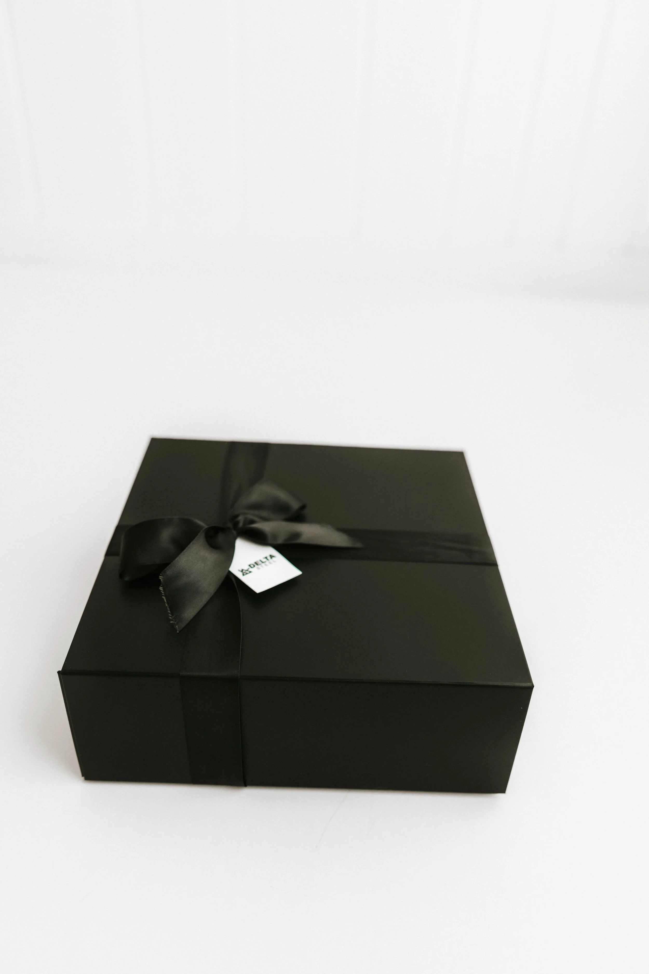 A black gift box with a satin ribbon and bow, placed on a white surface.