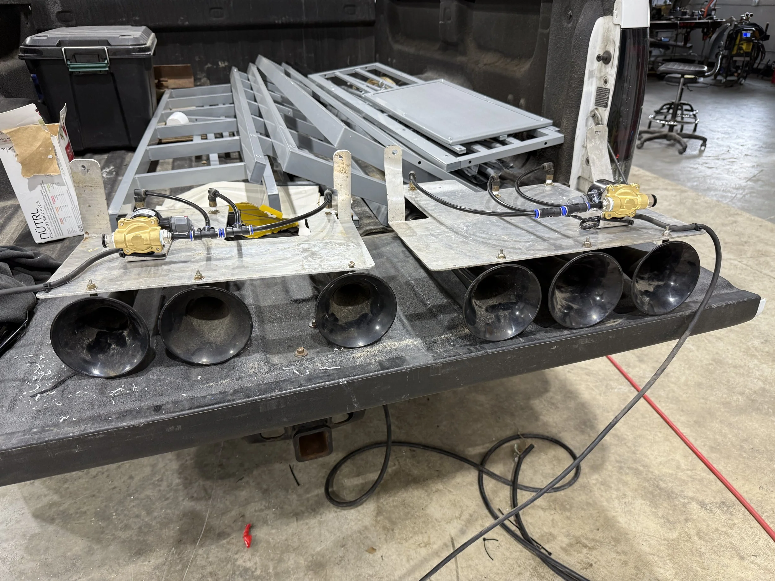 Multiple black megaphone-shaped speakers and metal components with wiring and yellow valves on a black work table in a workshop.