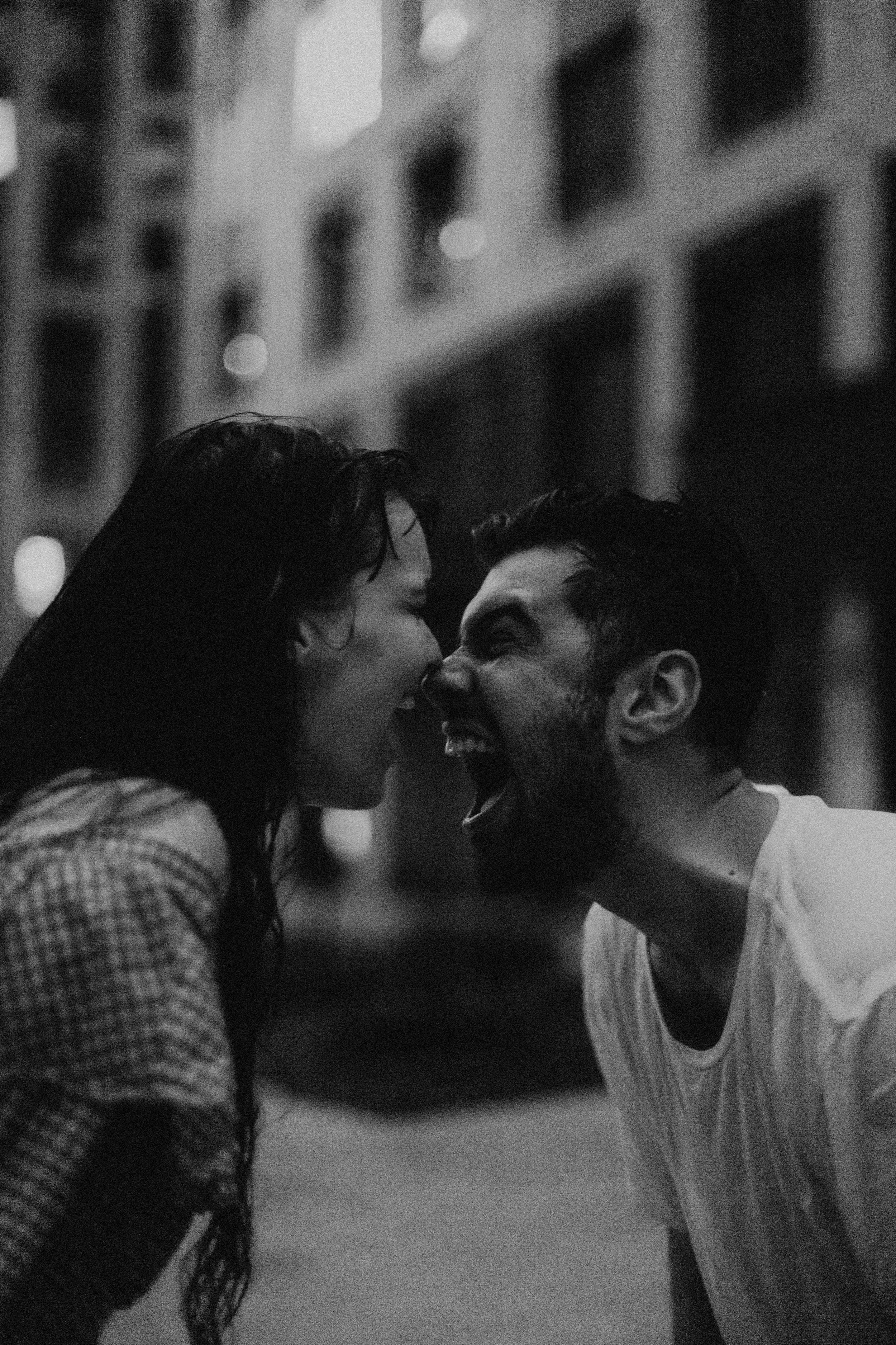A black and white photo of a man and woman outside at night, both laughing and touching noses.