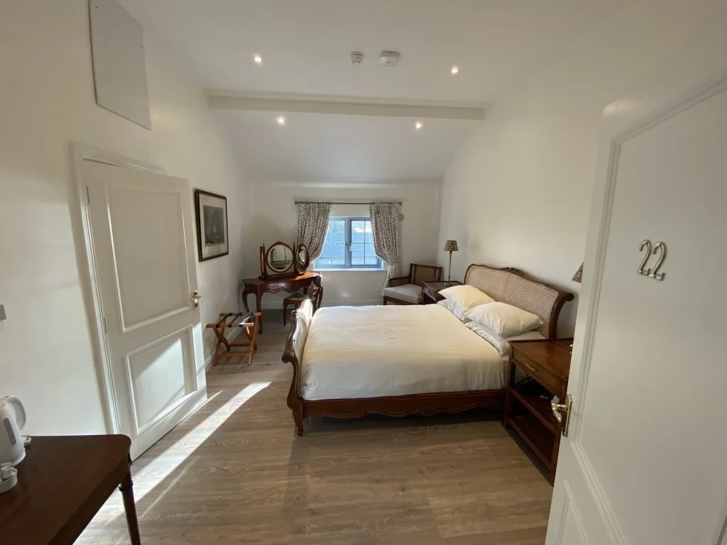 A cozy hotel room with a large bed, wooden furniture, a window with curtains, and classic decor.