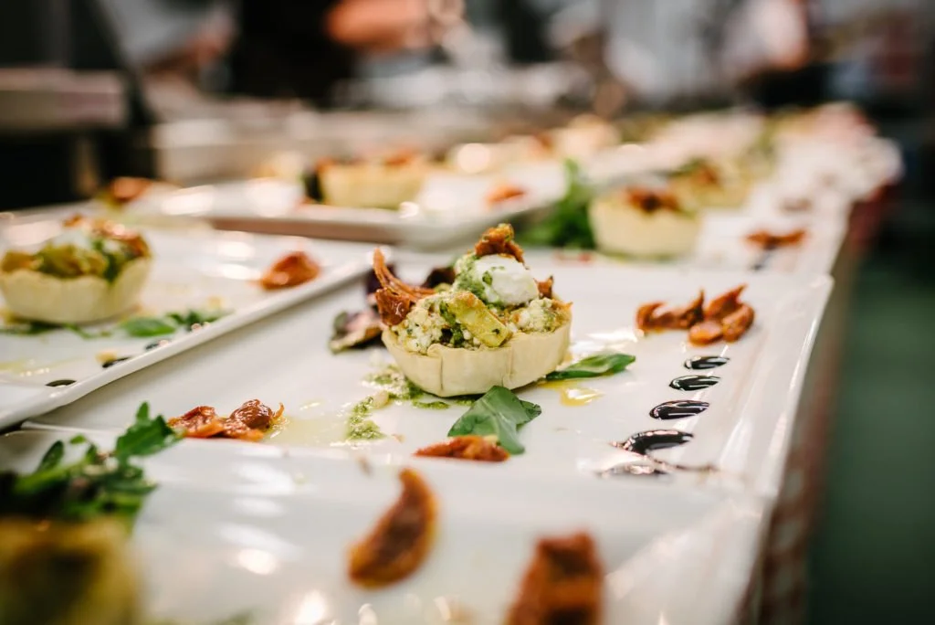 Close-up of a plated appetizer with a small pastry shell filled with creamy mixture, garnished with herbs and sauce, on a white platter.