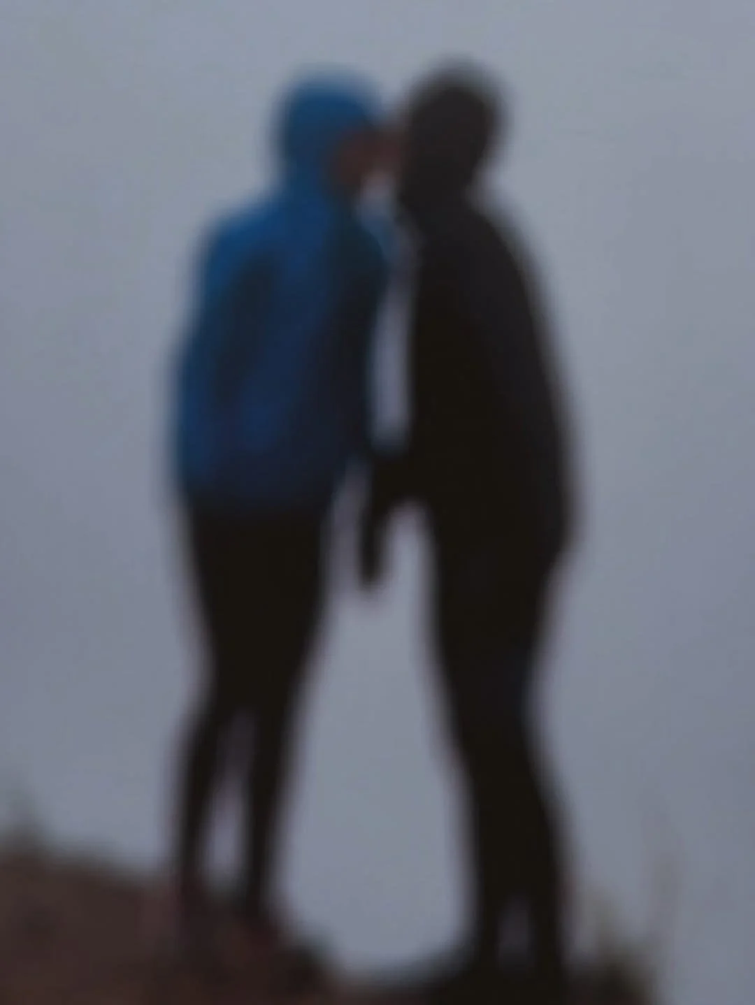 Two people holding hands, walking together outdoors in foggy weather, one wearing a blue jacket and the other a black jacket.