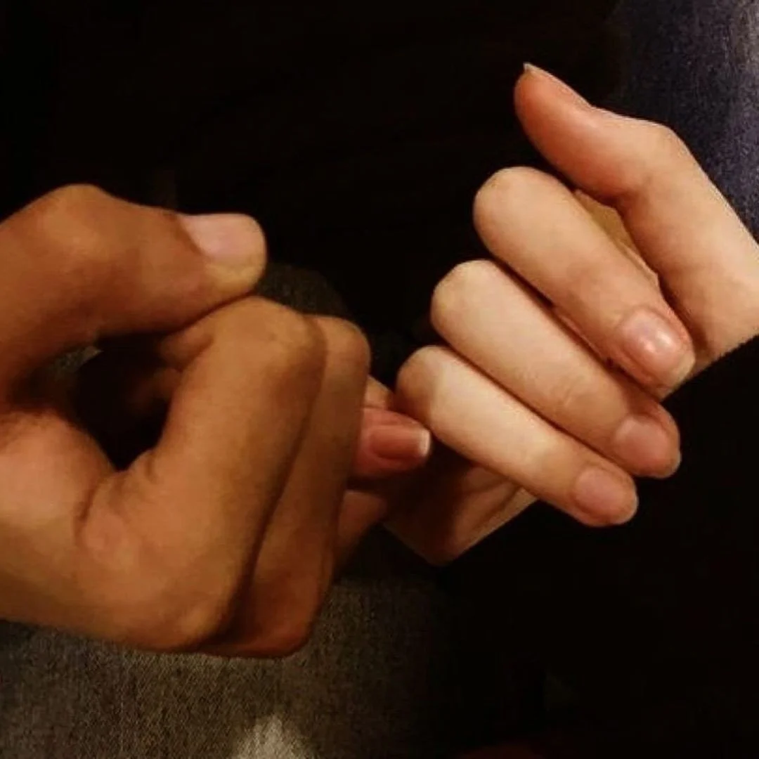 Close-up of two hands holding each other, one with darker skin and the other with lighter skin.