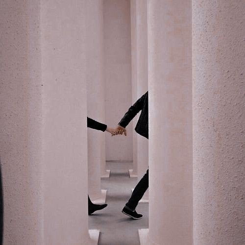 Two people holding hands, seen through narrow gaps between pink walls.