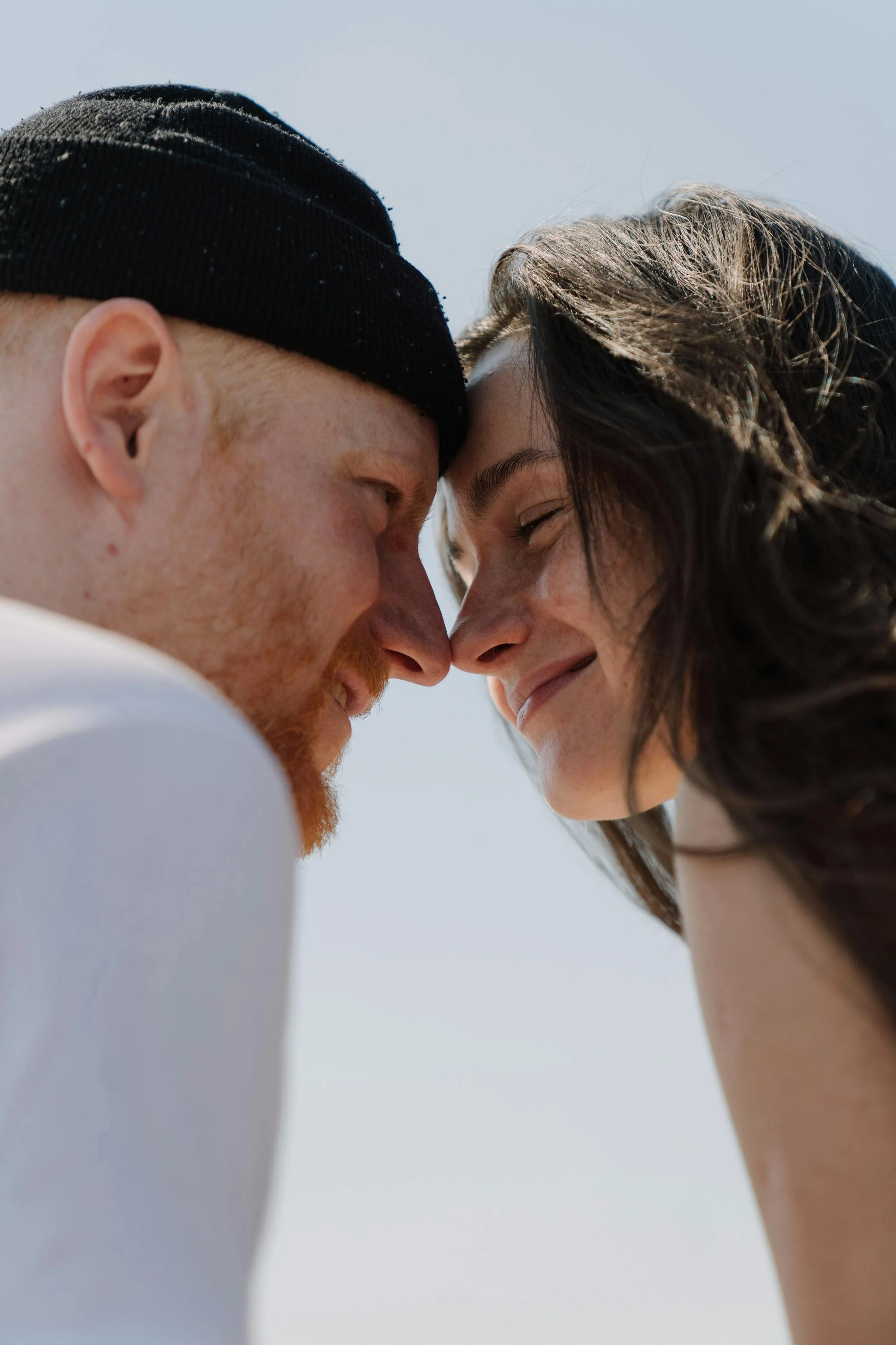 Close-up of a couple with foreheads touching, smiling, outdoors on a sunny day.