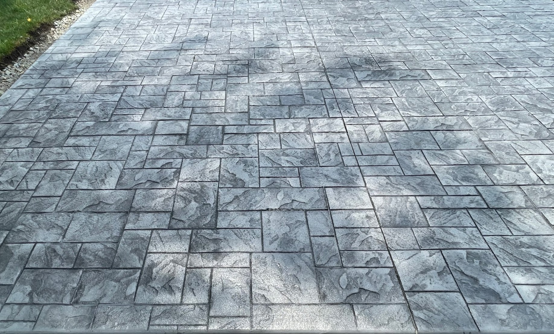 Grey stone patterned sidewalk with a slight gradient and greenery on the left edge.