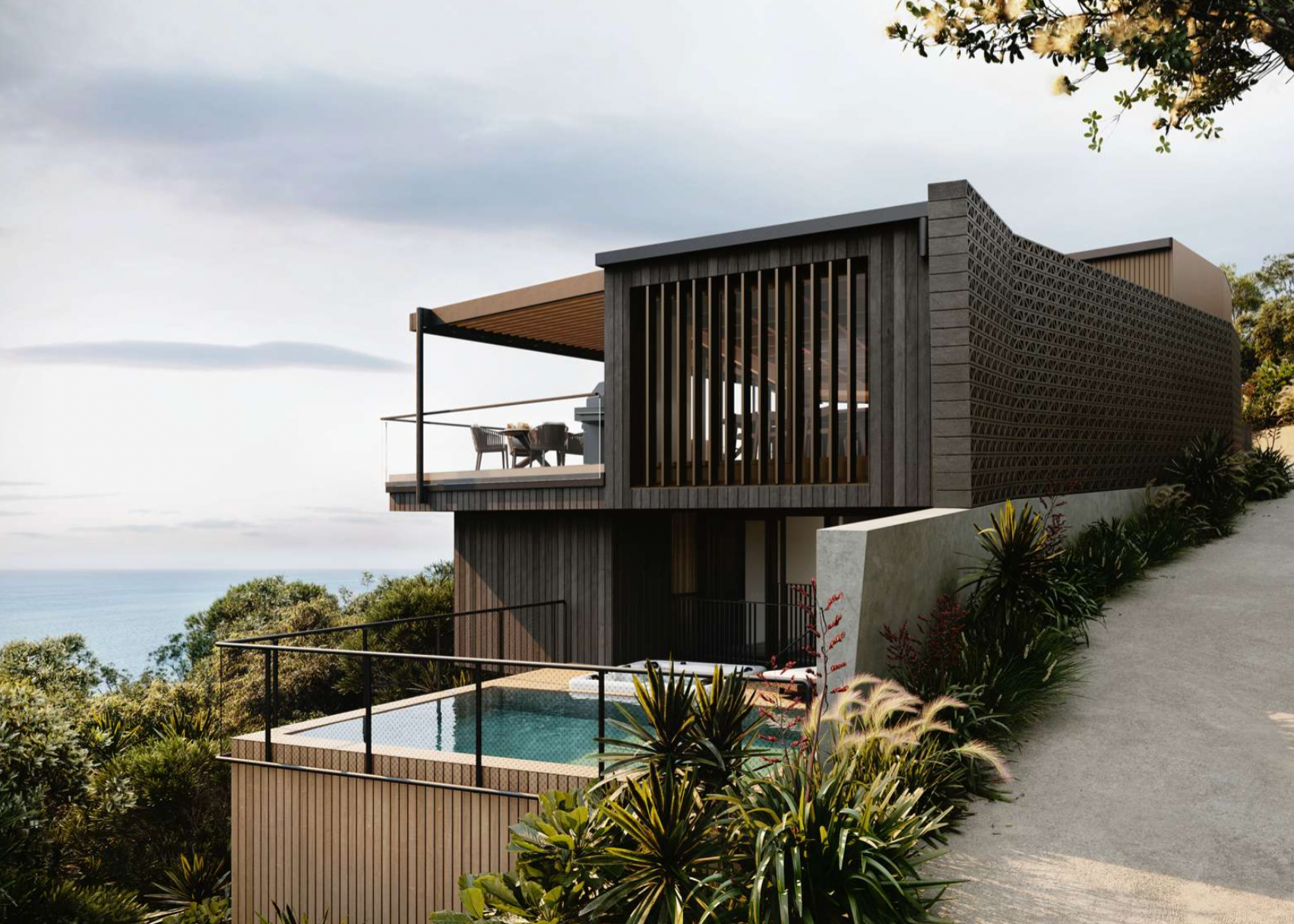Modern two-story house with a terrace, outdoor dining area, and a small pool, overlooking a lush landscape and ocean, with cloudy sky overhead.