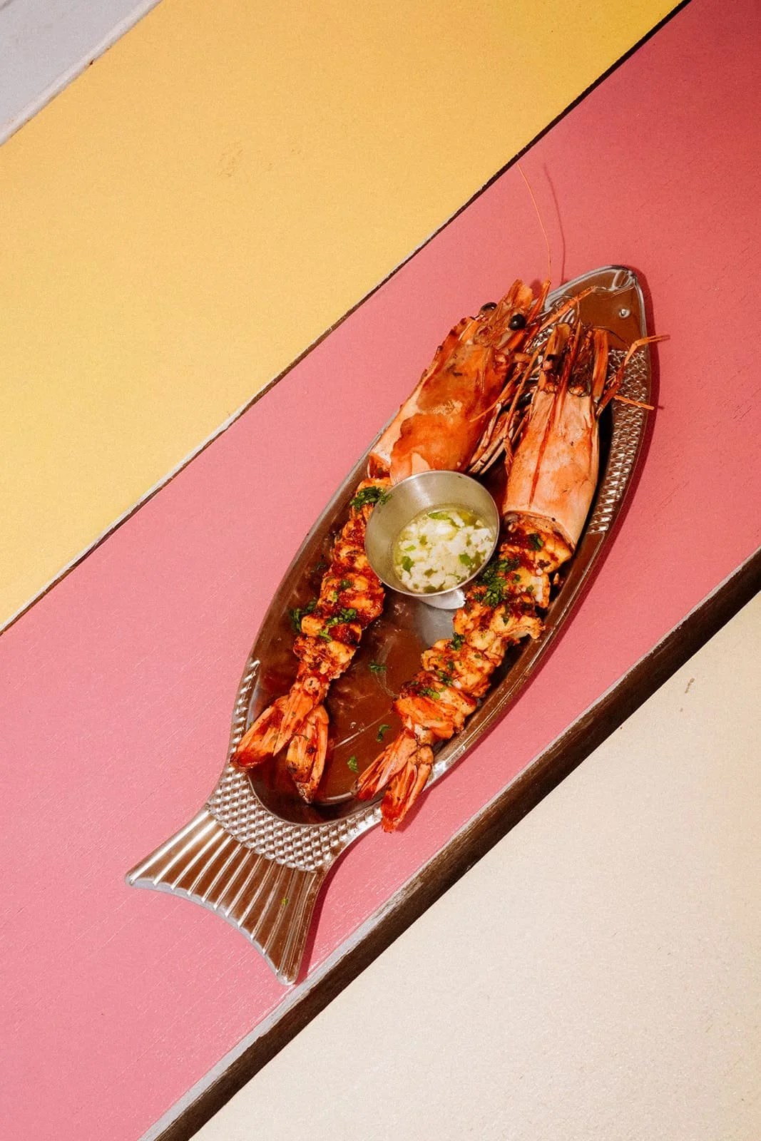 Grilled whole head-on prawns served with dipping sauce on a fish-shaped platter at Six Coasts on Governors Island.