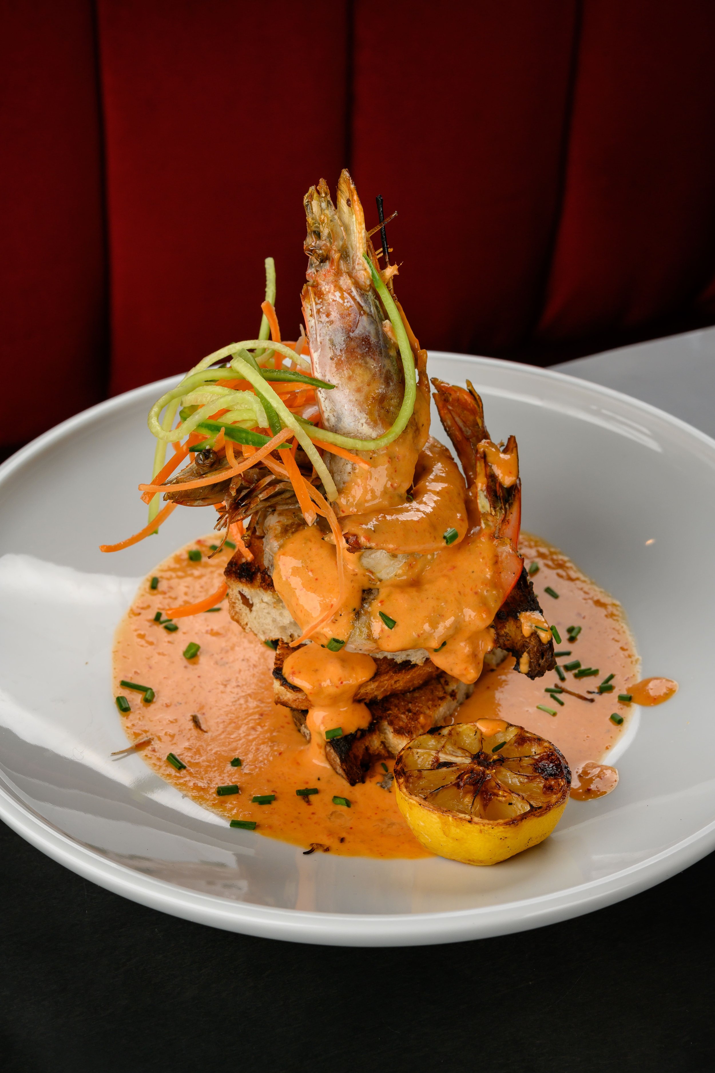 Seafood dish with shrimp, grilled lemon, and vegetable garnish in a creamy sauce on a white plate.