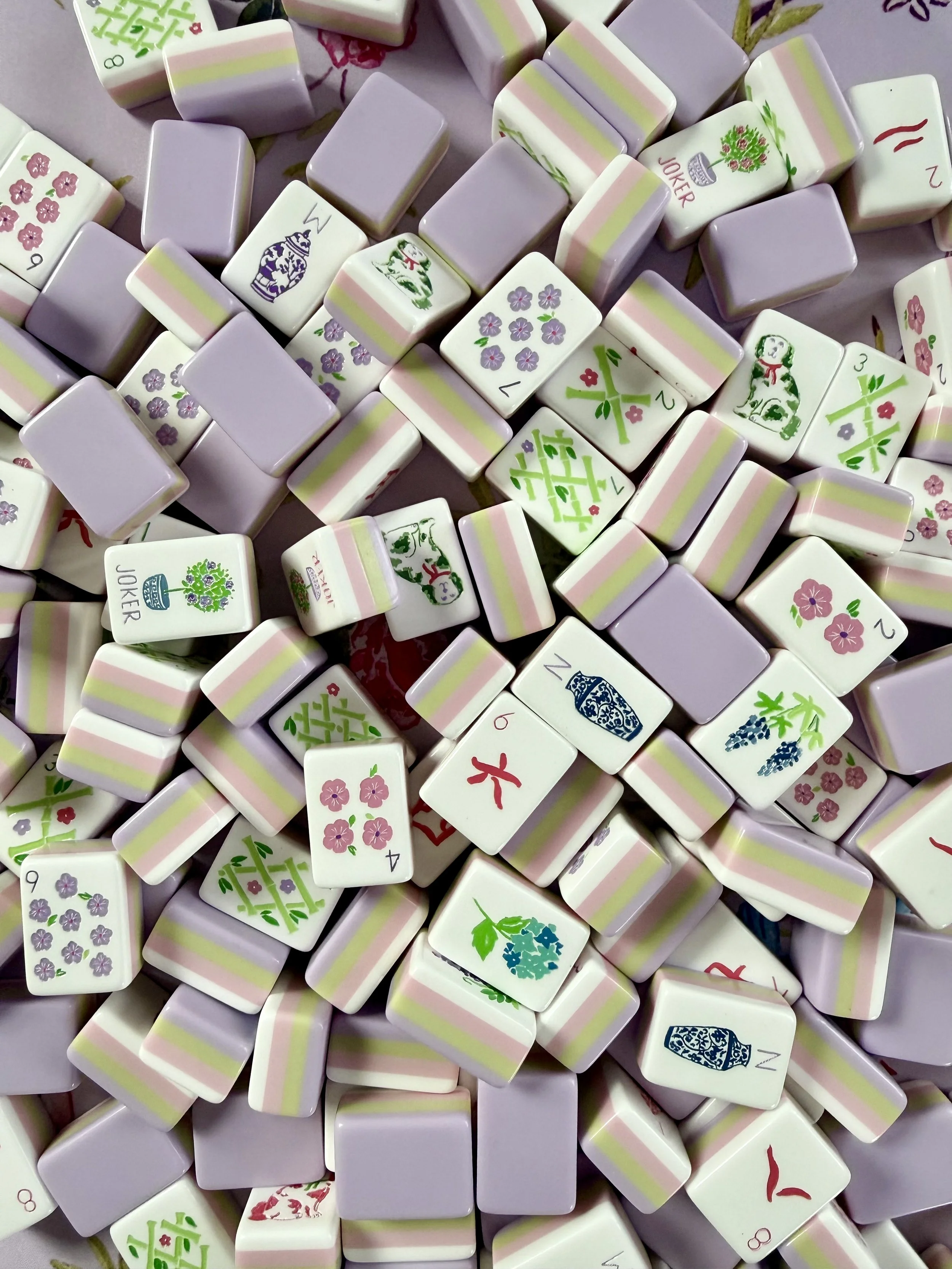 A collection of Mahjong tiles with floral, bamboo, and character designs in pastel colors.