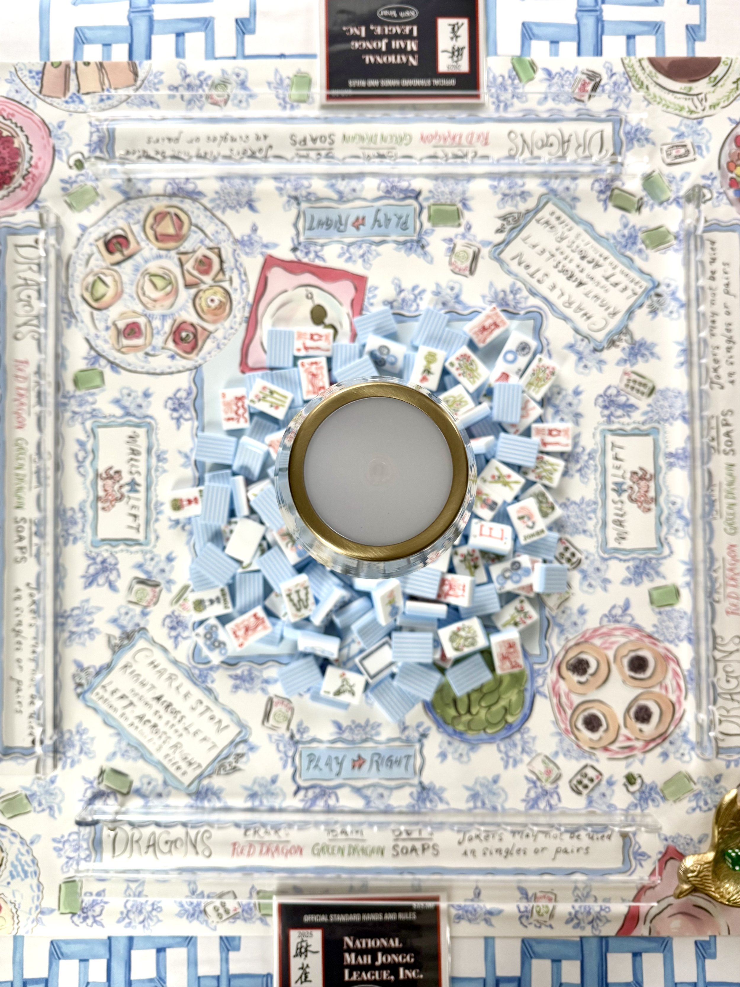 A colorful board game with a tea cup in the center, featuring various tiles, cards, and game pieces laid out on the board. The game appears to involve themes of dragons, teas, and storytelling.
