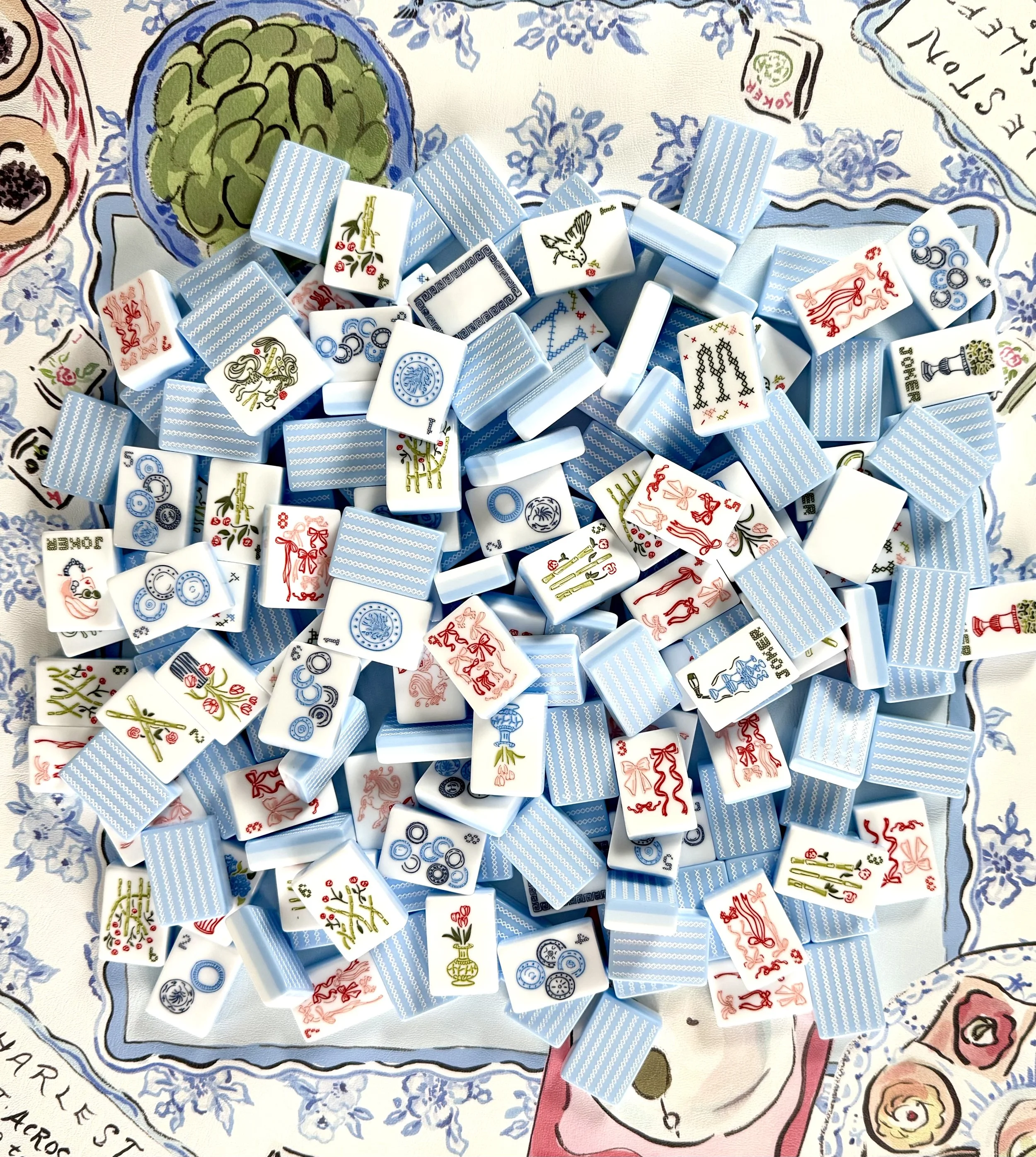 A pile of domino tiles with blue backs and various decorated faces, spread out on a patterned cloth.