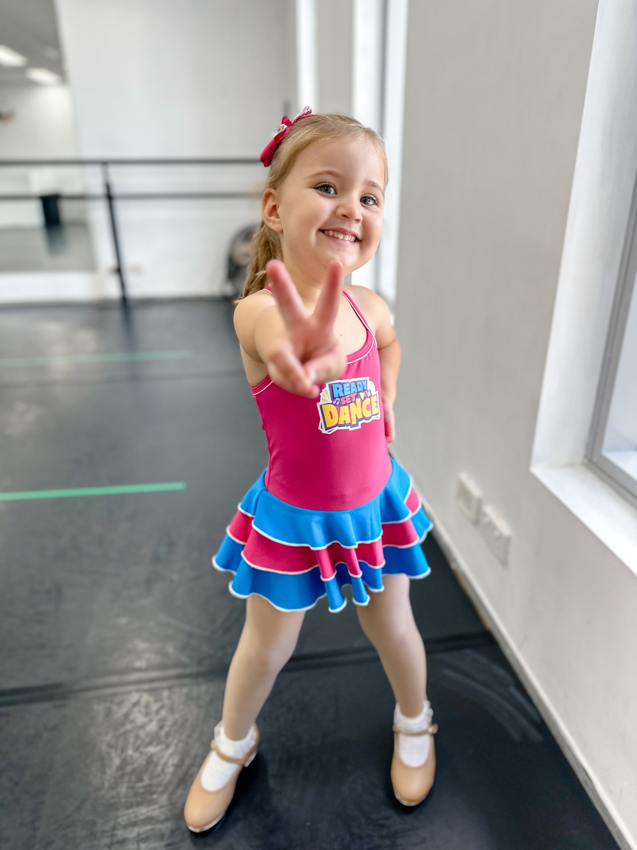 Young girl in colorful dance costume making a peace sign and smiling.