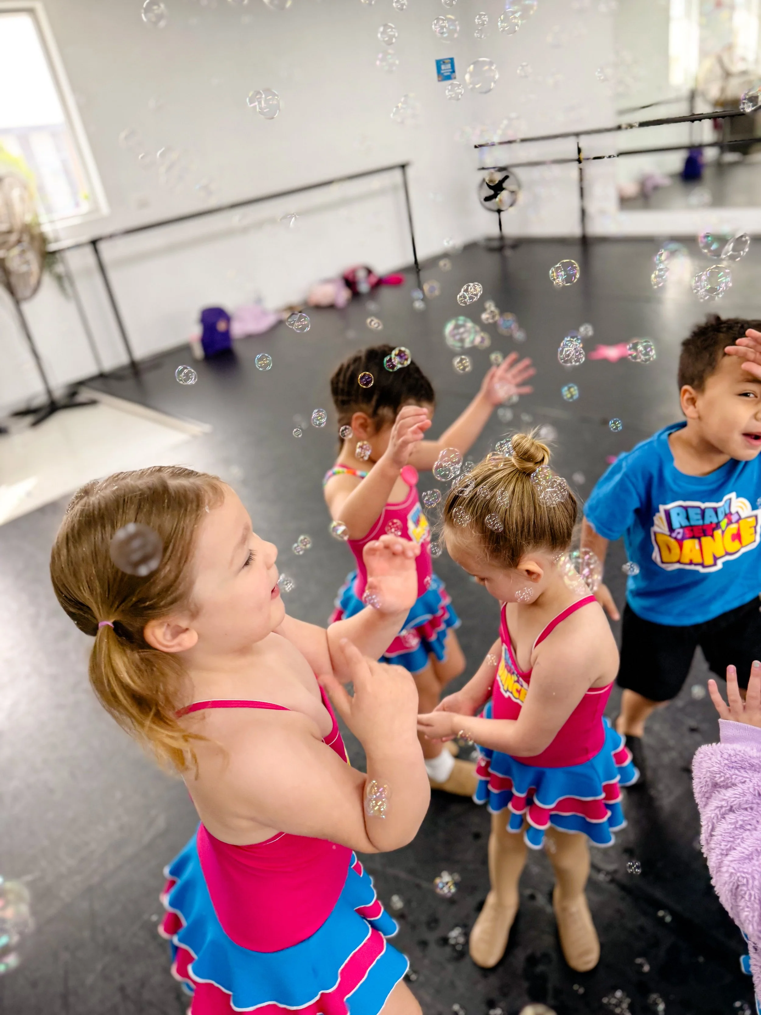 Children in colorful dance costumes playing with bubbles in a dance studio.
