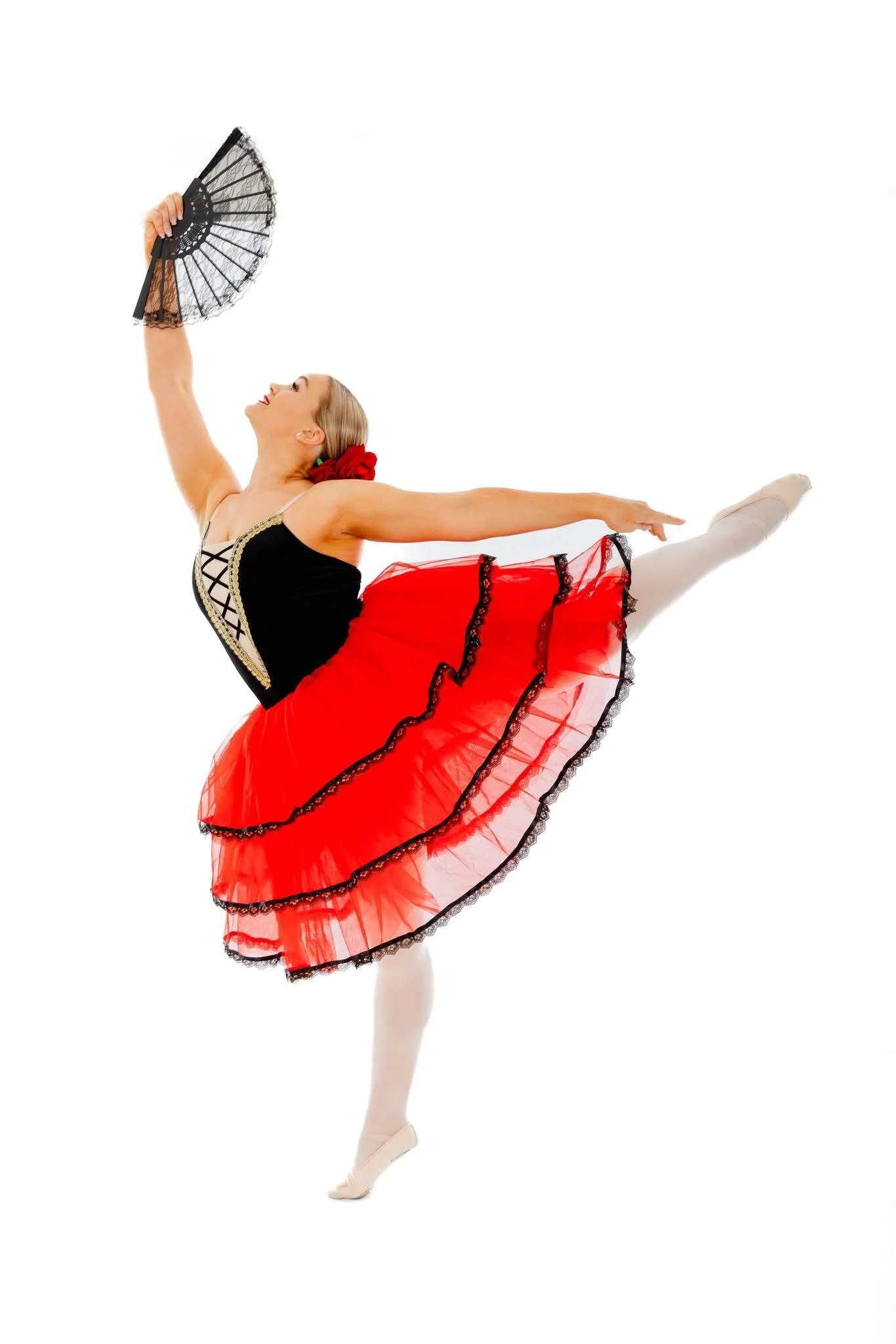 Ballet dancer in a red tutu and black top performing a pose with a fan against a white background.