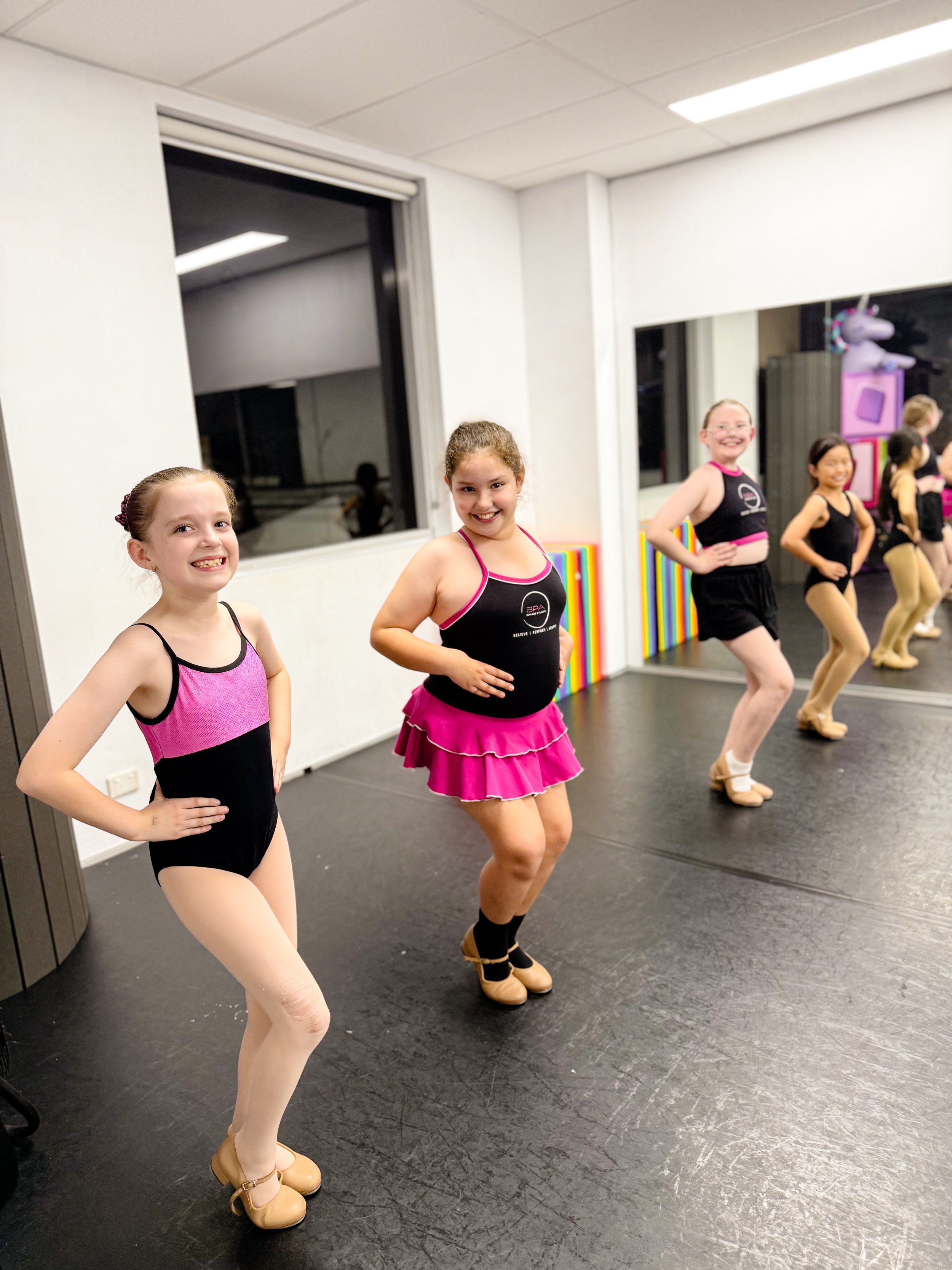 Group of young girls practicing ballet in a dance studio, wearing ballet costumes and toe shoes.