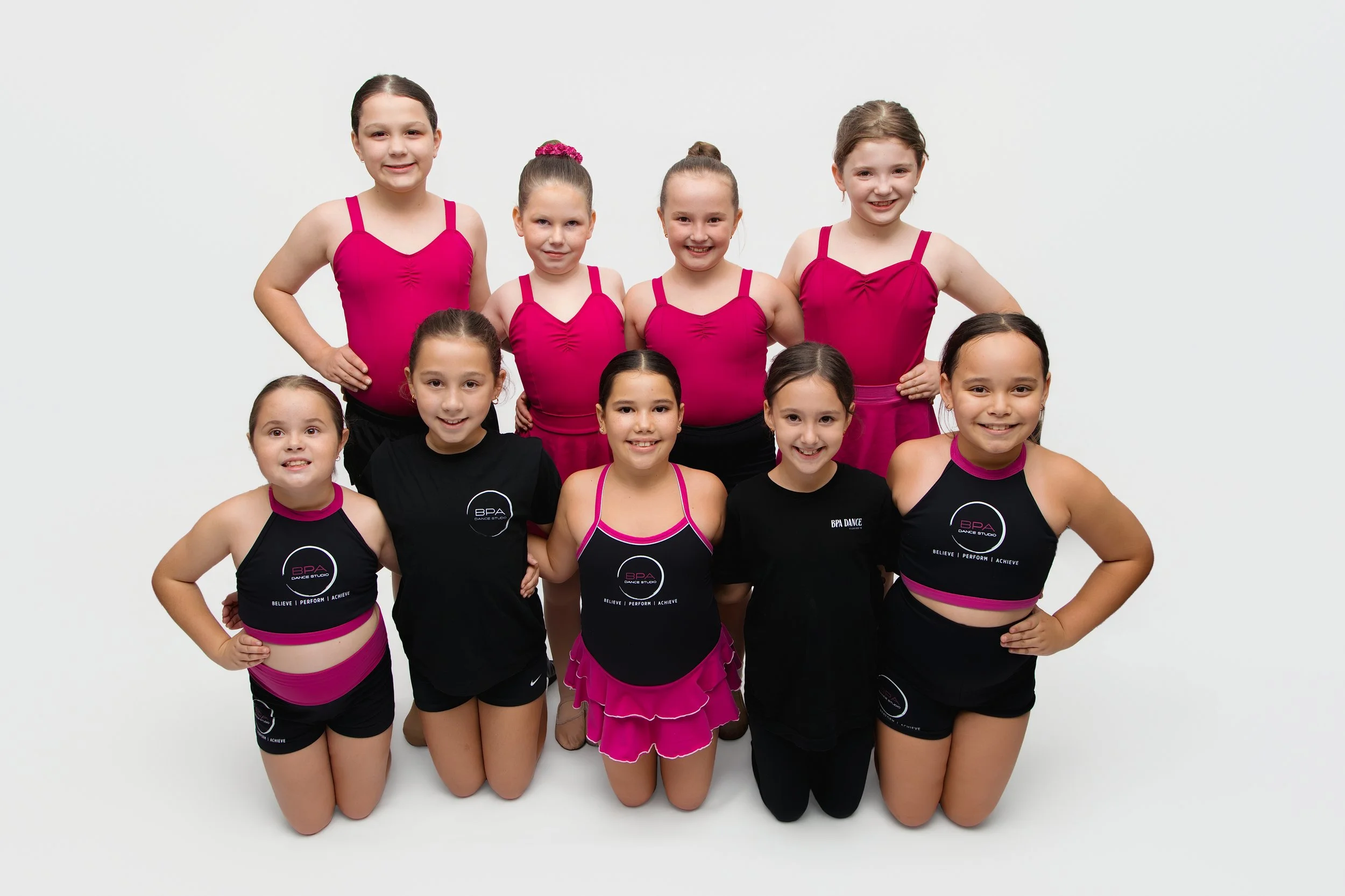 Group of young girls in dance costumes posing together against a white background.