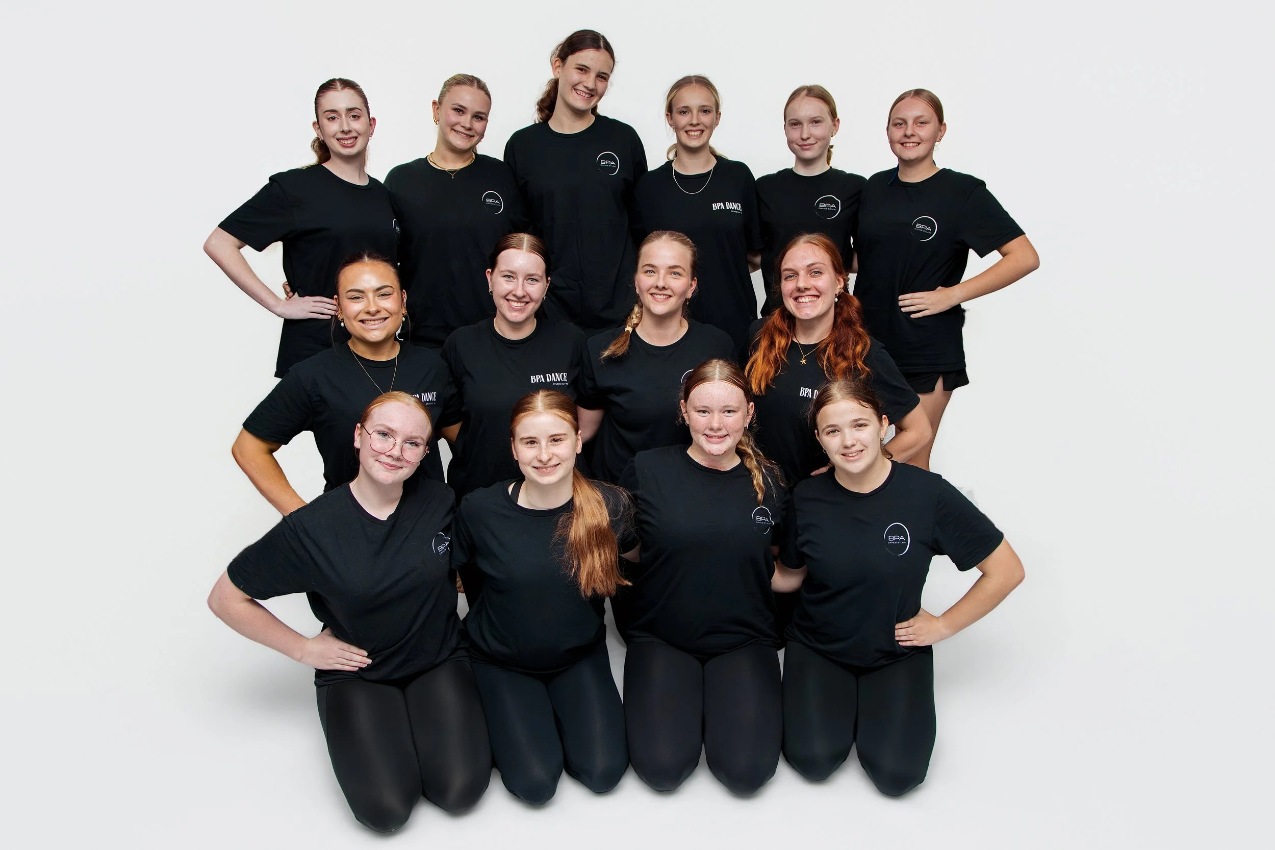 Group of young women in matching black T-shirts posing together against a white background, smiling at the camera.