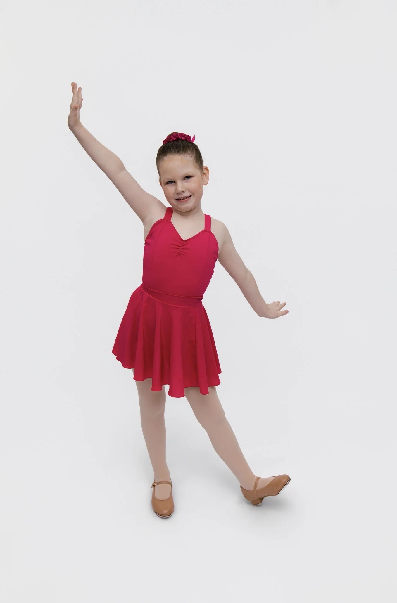 Young girl in a red ballet dress and tan ballet shoes practicing ballet on a white background.