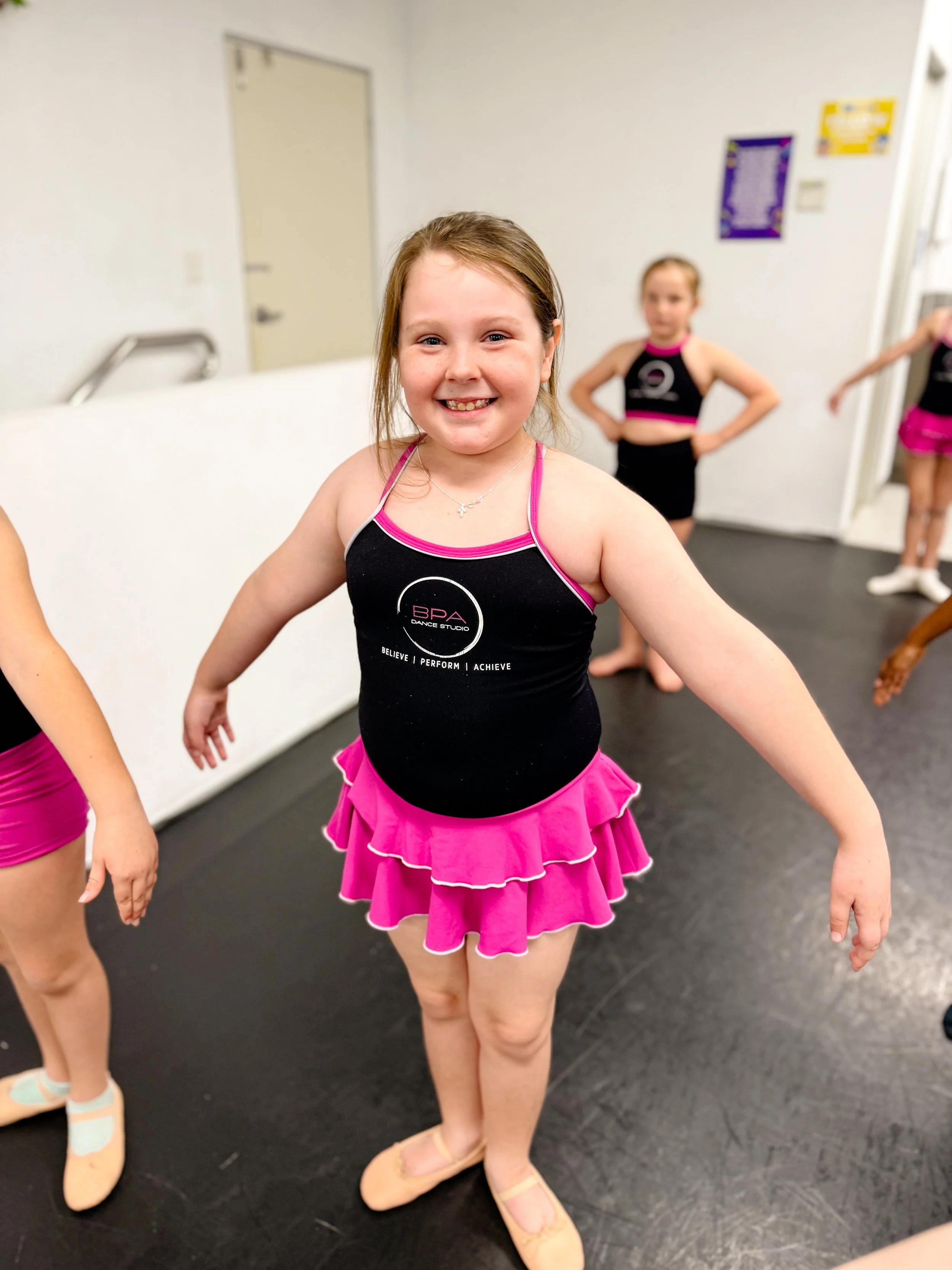 Smiling young girl in a pink cheerleading outfit standing in dance studio.