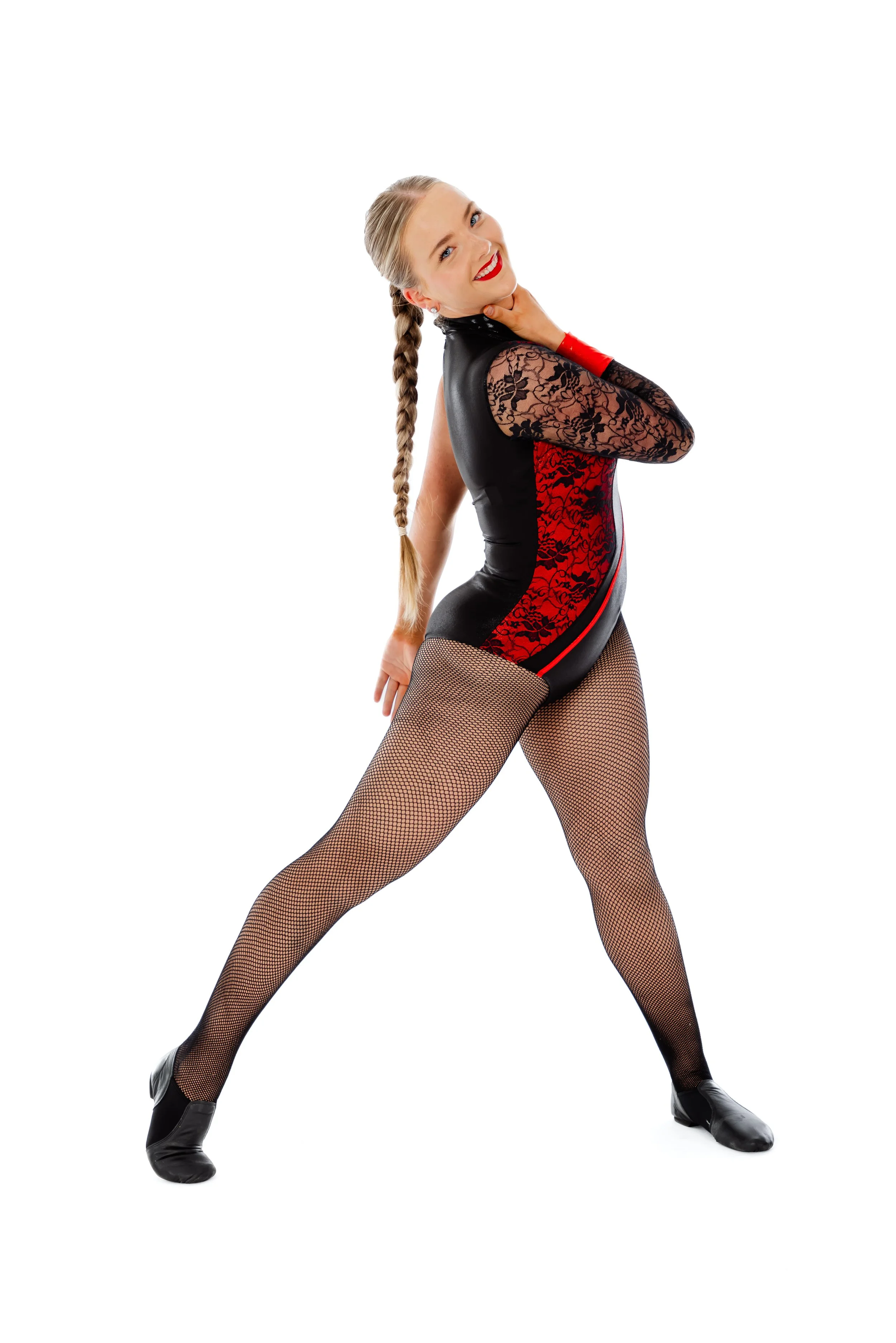 A woman smiling, striking a pose, wearing a black and red dance outfit with lace sleeves, fishnet stockings, and black dance shoes, standing against a white background.