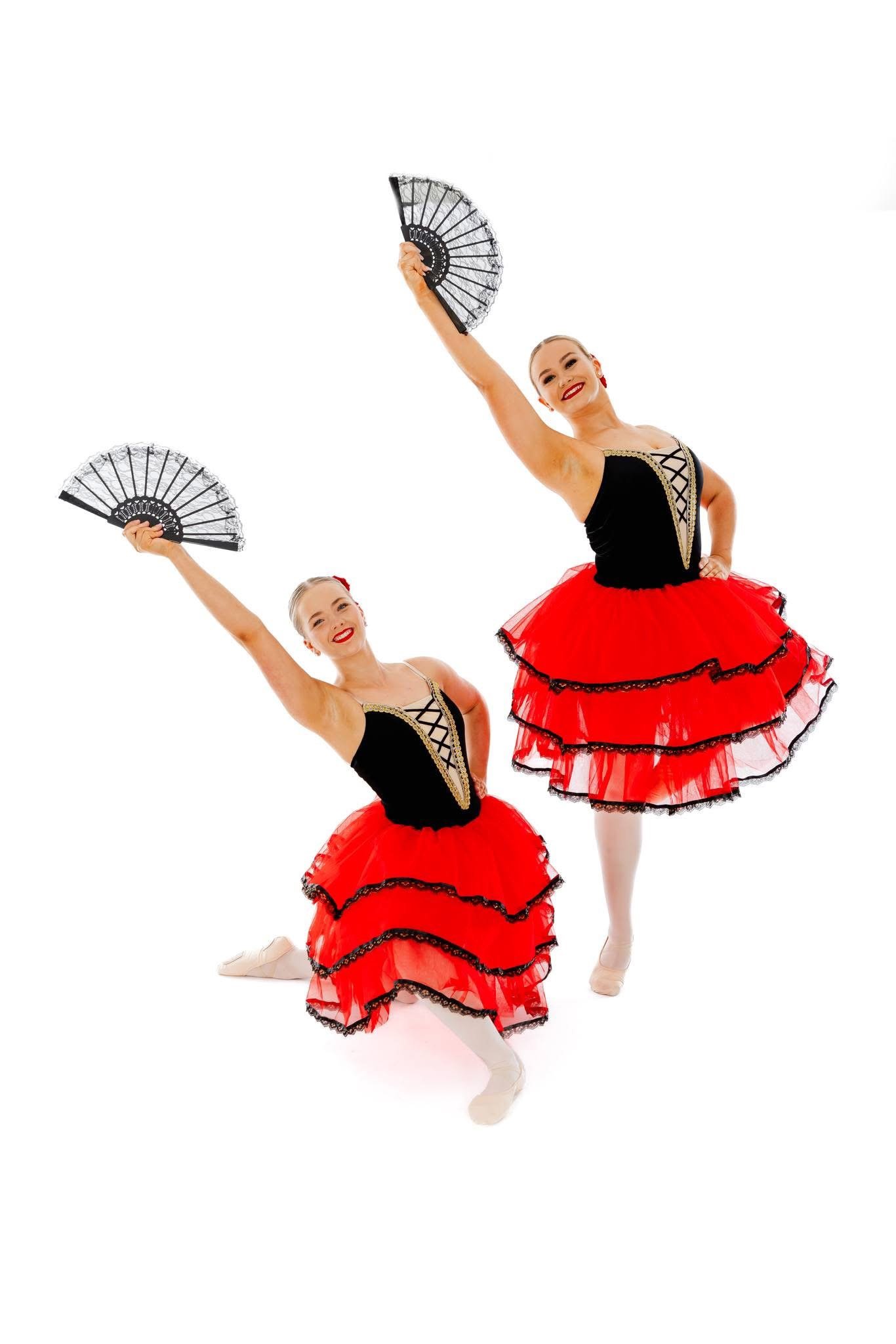 Two ballet dancers in red and black costumes holding fans, smiling, and striking dance poses against a white background.