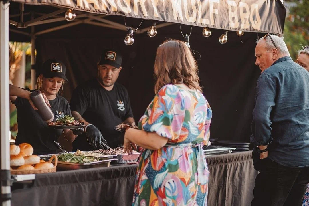 People ordering food at a barbecue food stand at an outdoor event.