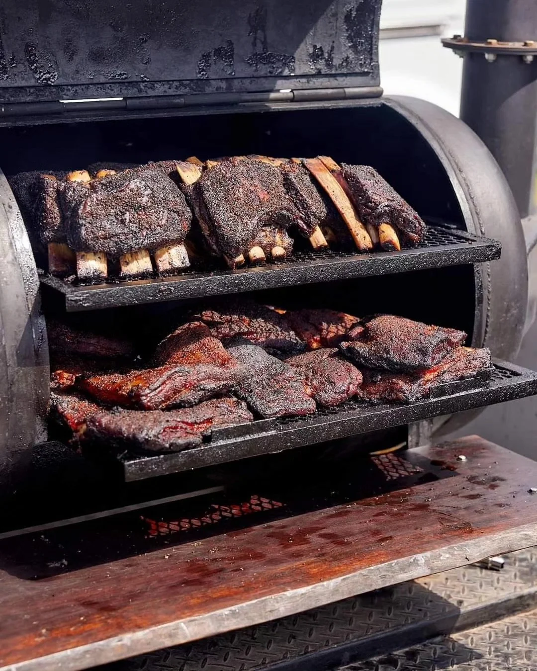 Barbecue smoker with racks of smoked beef ribs in a barbecue smoker.