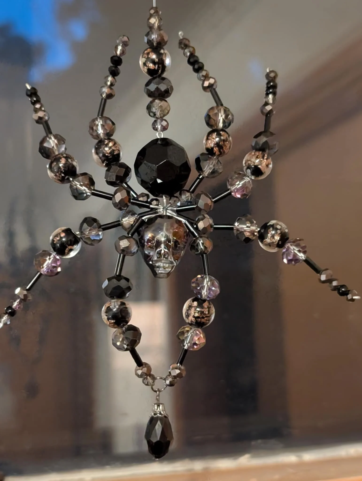 Decorative hanging ornament with black and clear beads, skull-shaped centerpiece, and a black teardrop-shaped pendant.