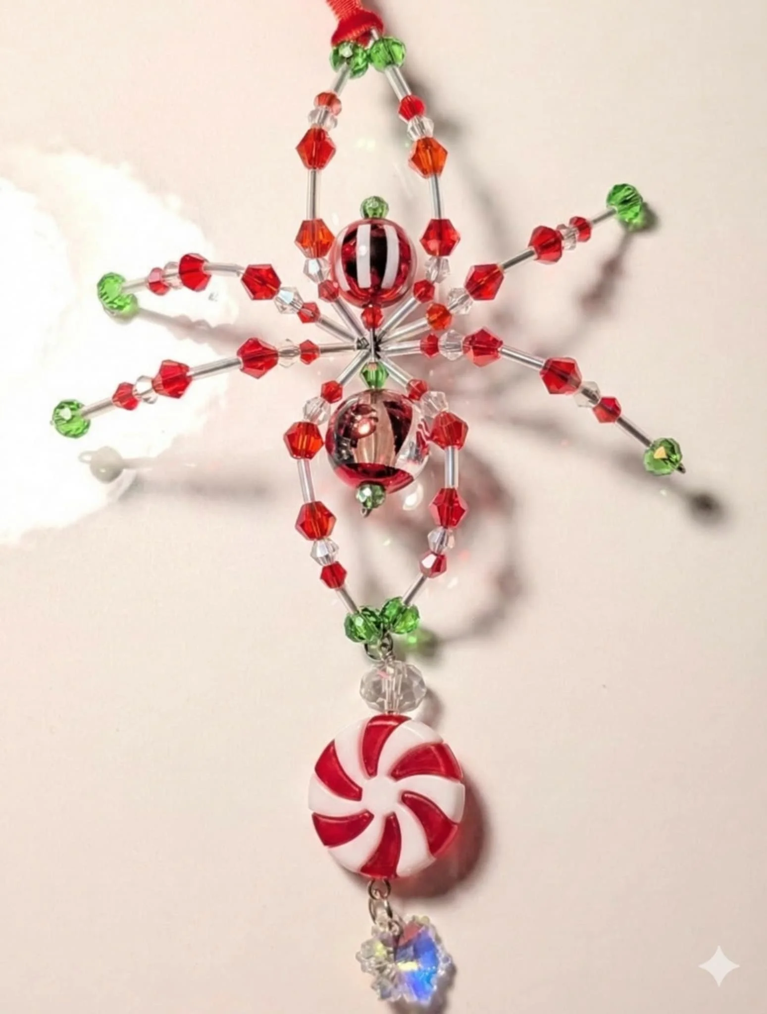 Holiday ornament decorated with red, green, and clear beads, featuring a peppermint candy pendant and a small star-shaped charm.