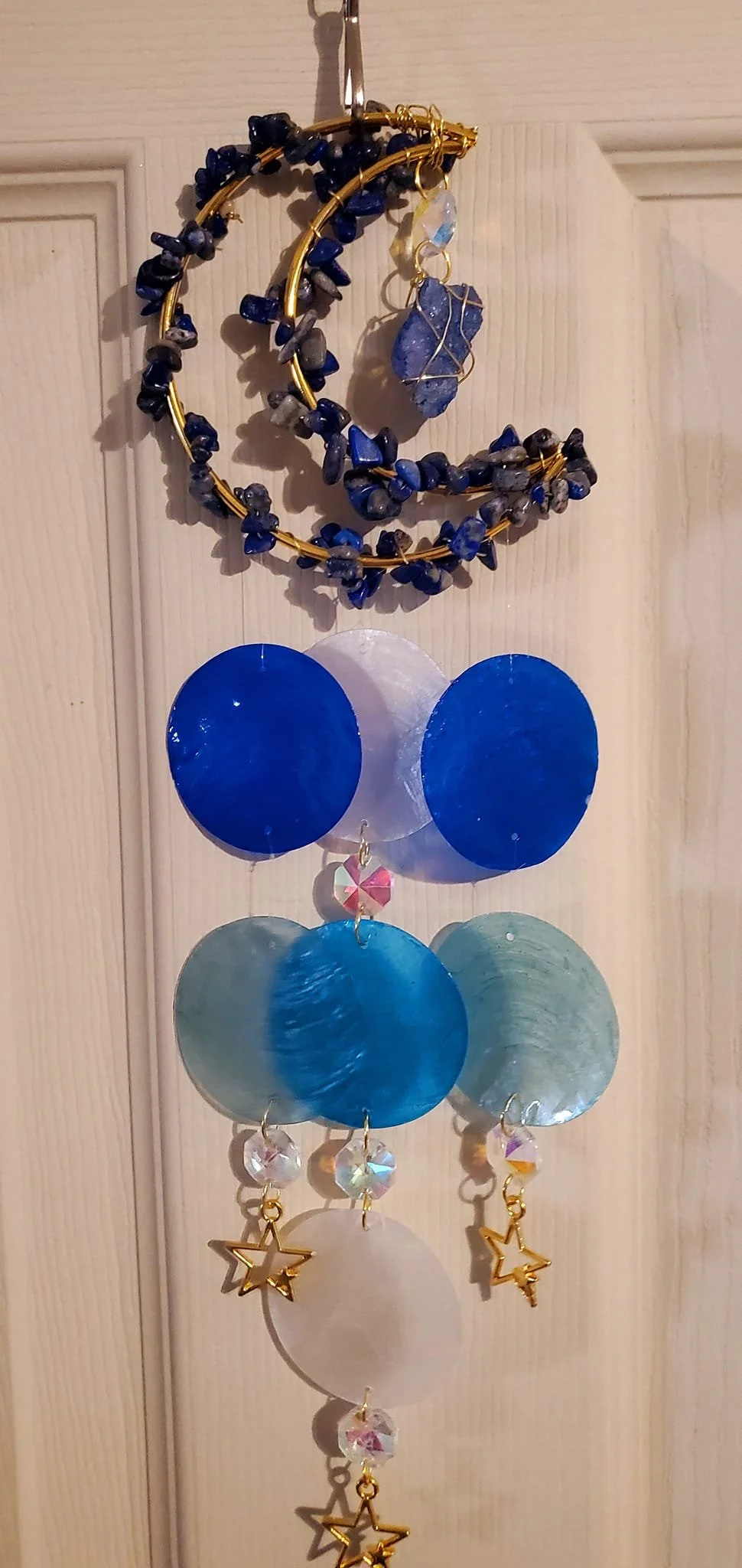 Decorative hanging ornament made of various blue, white, and clear circular and star-shaped beads and stones, with a ruched blue stone in the middle.