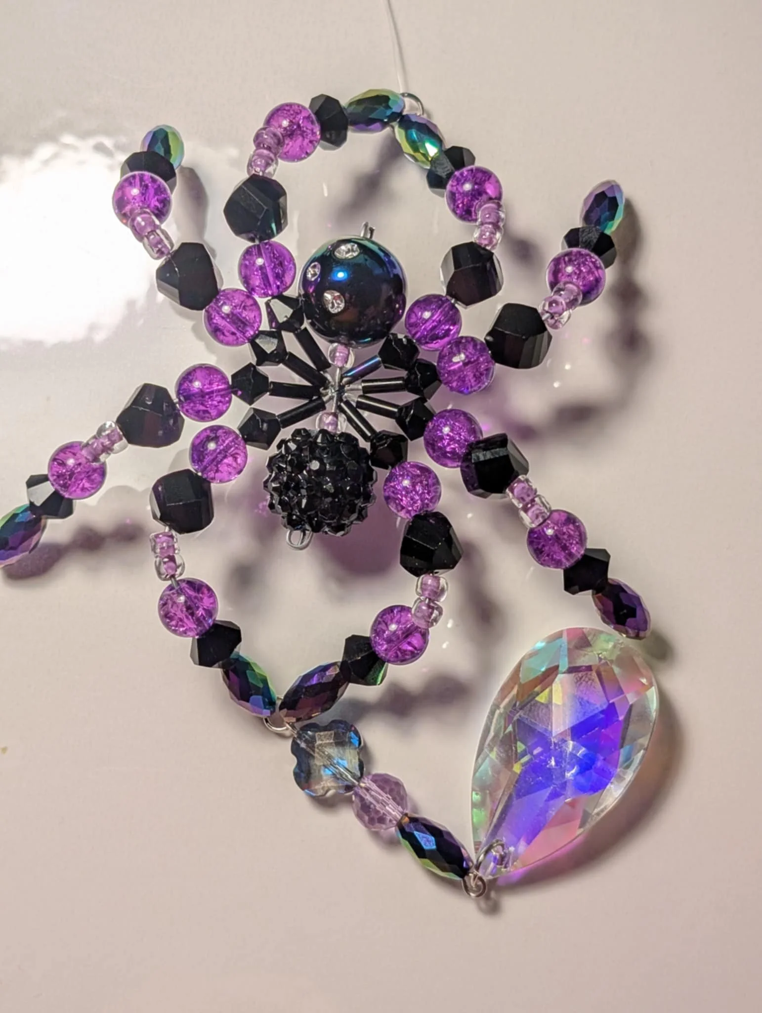 Colorful beaded necklace with purple, black, and iridescent beads, featuring a large teardrop-shaped crystal pendant.