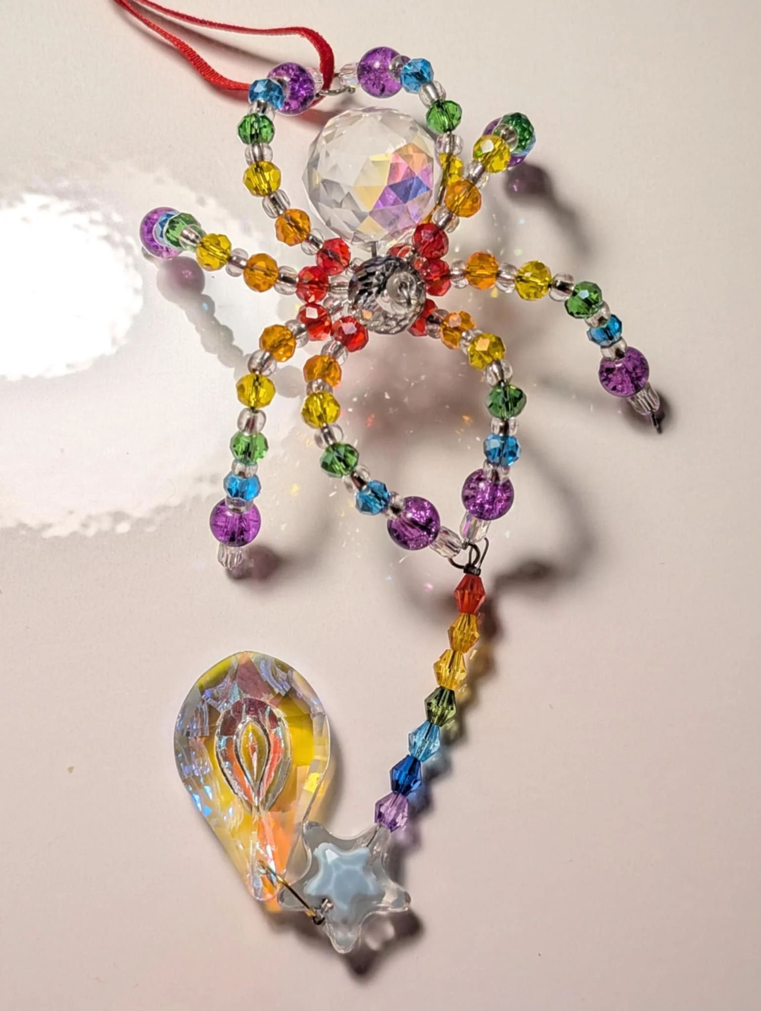 Colorful beaded rainbow-shaped ornament with a large faceted crystal and a star-shaped charm at the bottom.