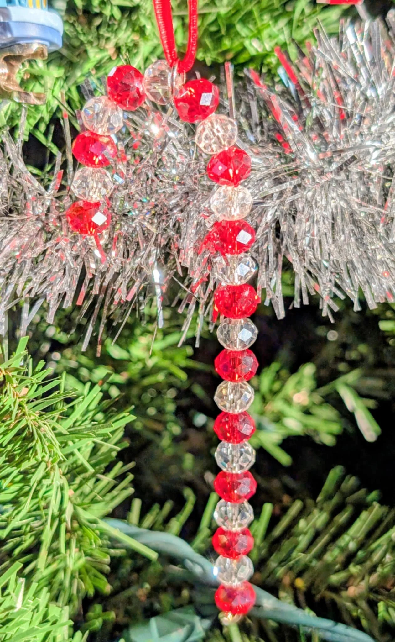 Close-up of a Christmas ornament with red and clear beads hanging from a decorated Christmas tree.