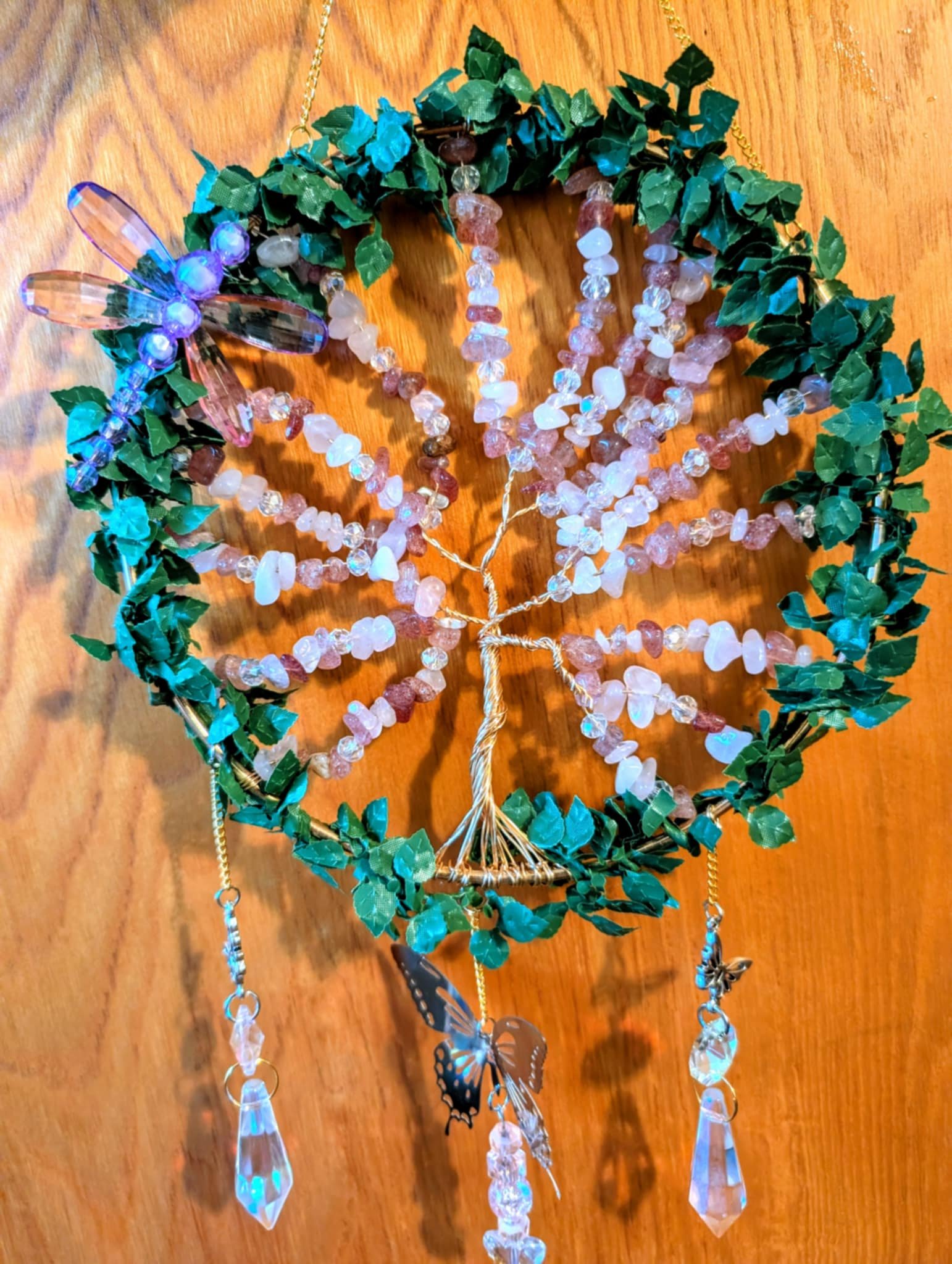 Decorative wall hanging featuring a wire tree with pink and clear beads, surrounded by a leafy green wreath with hanging crystal and butterfly ornaments and a purple LED-lit dragonfly.