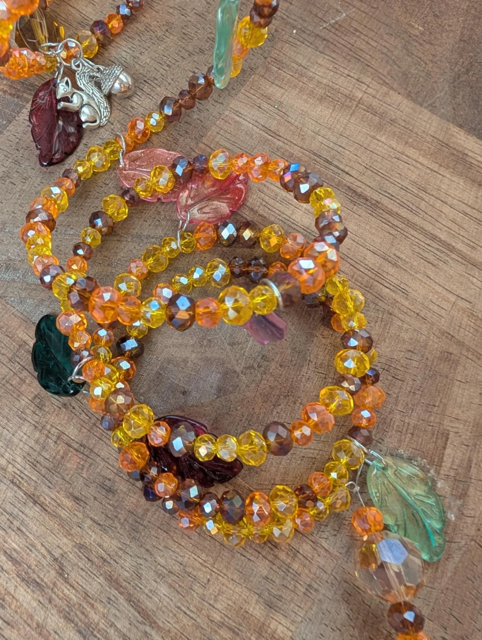 Colorful beaded jewelry with leaf and animal charms on a wooden surface.