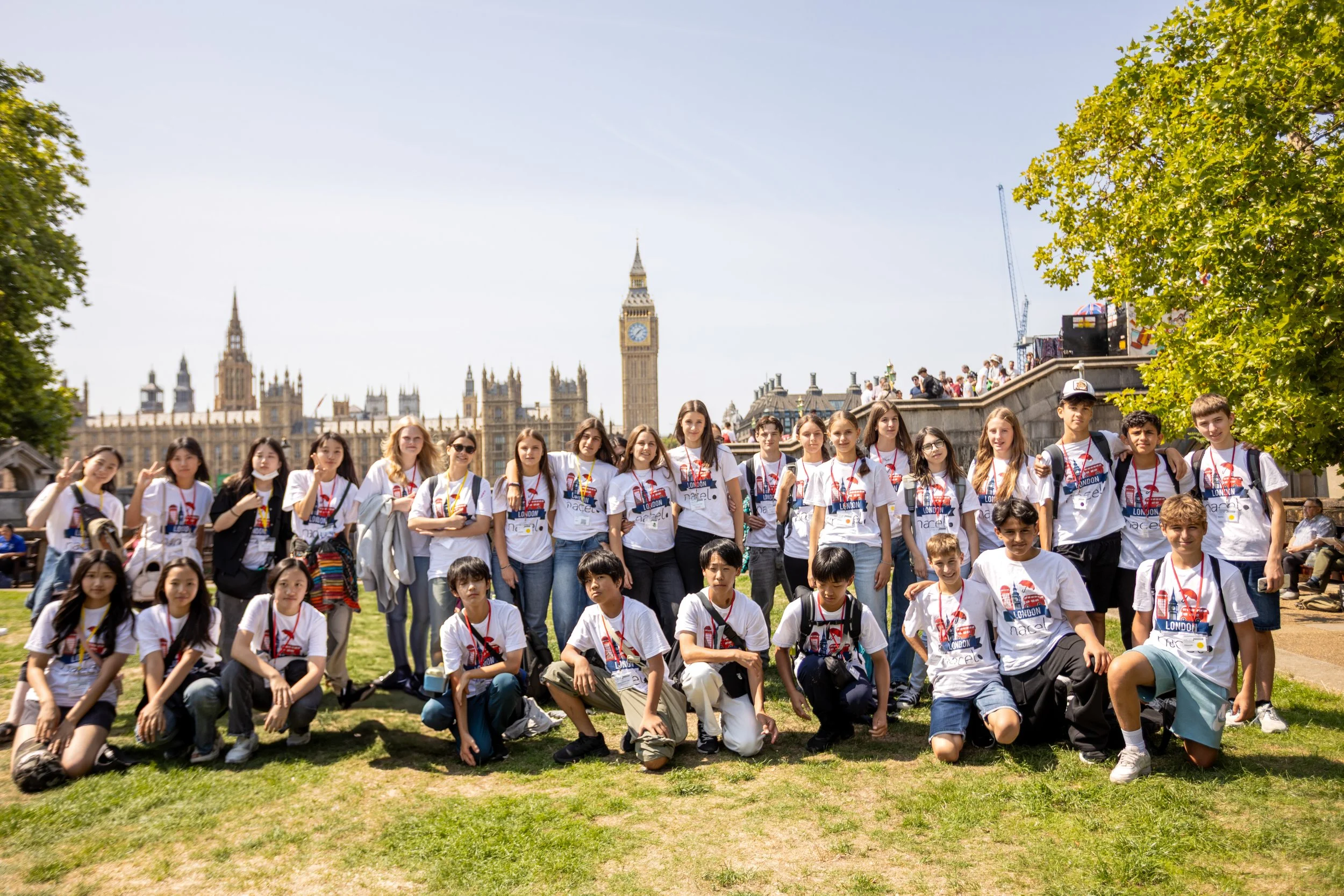 Group of children and teenagers outdoors in front of the UK Parliament with Big Ben, wearing matching white T-shirts and red lanyards.