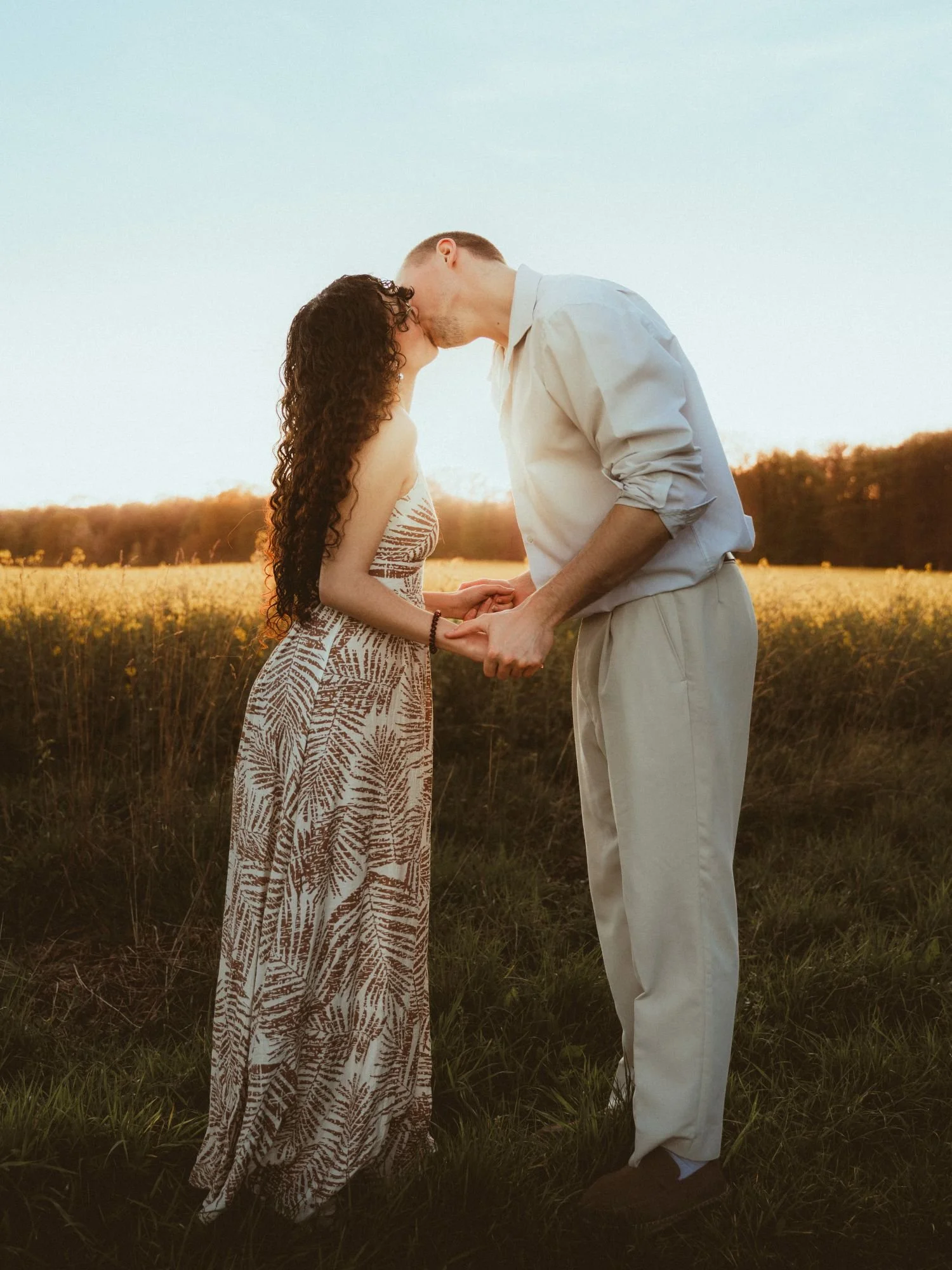 Un couple s'embrasse dans un champ lors du coucher du soleil.